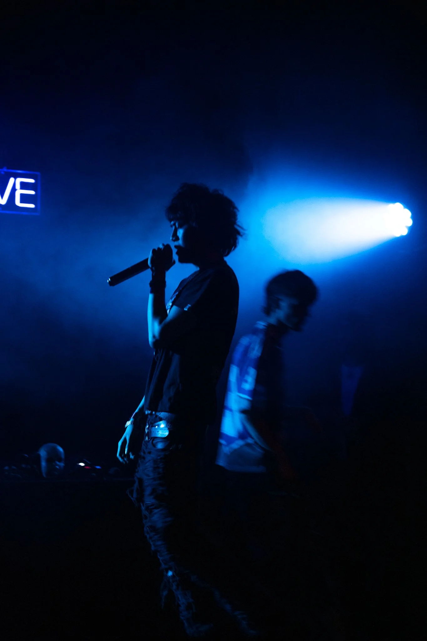 Silhouette of a person holding a microphone on stage with blue lighting in a dark room.