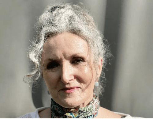 Close-up of an older woman with curly gray hair, wearing a colorful scarf around her neck, standing outdoors.