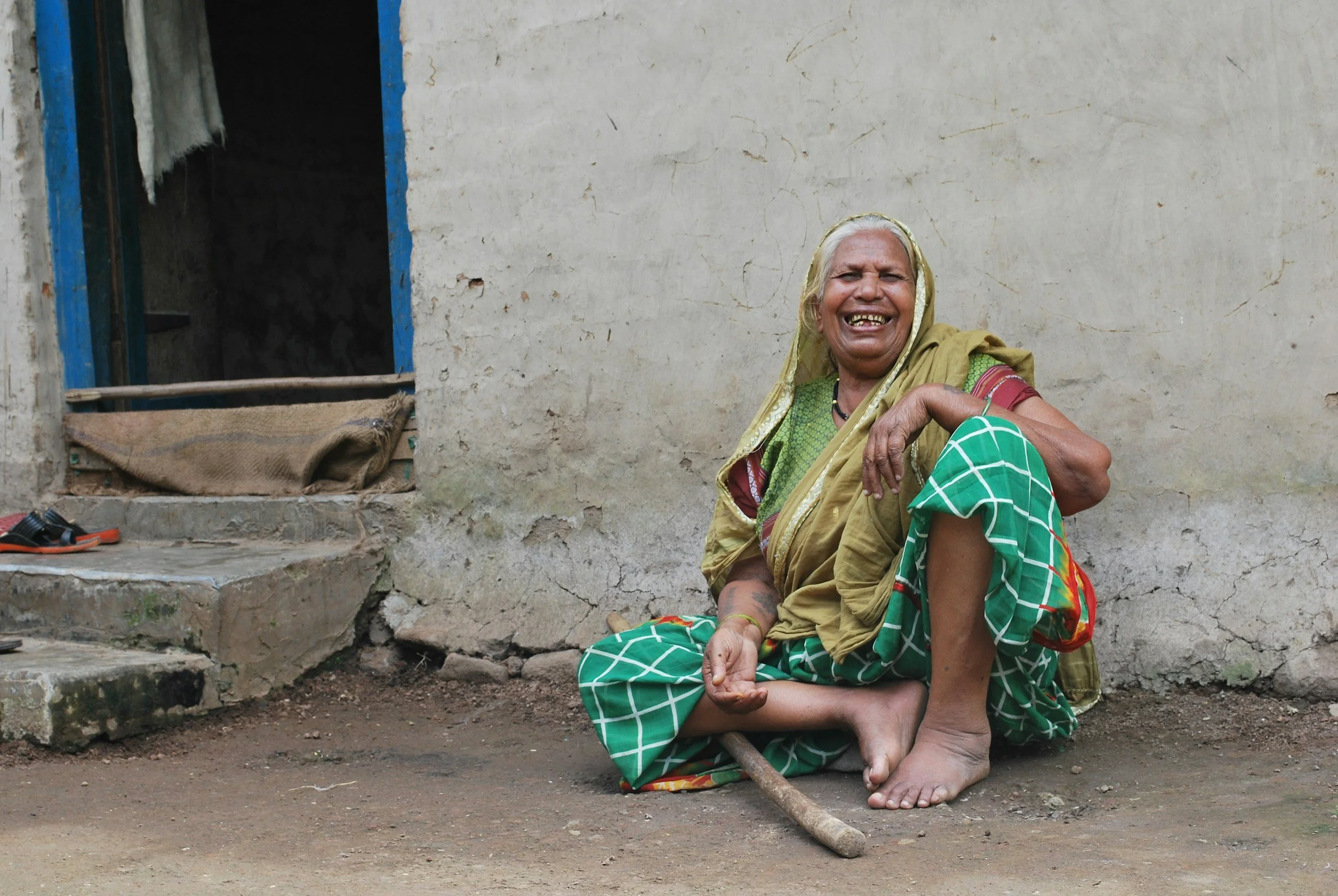 Older Indian woman seated outside her home, smiling warmly