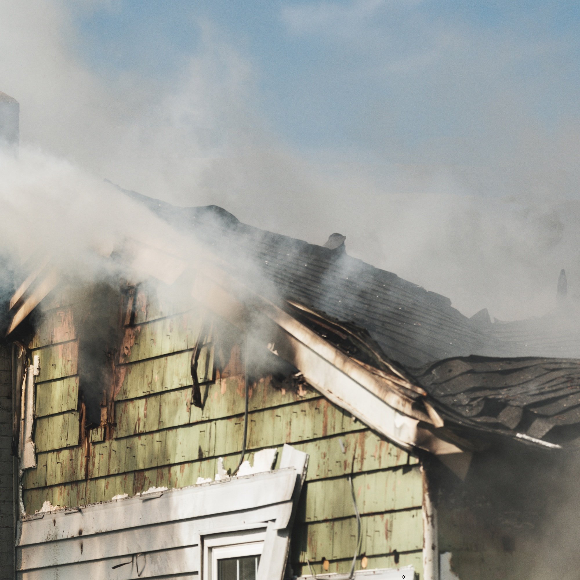 Burnt wooden fence or wall with charring, smoke, and debris, likely from a fire or fire damage.