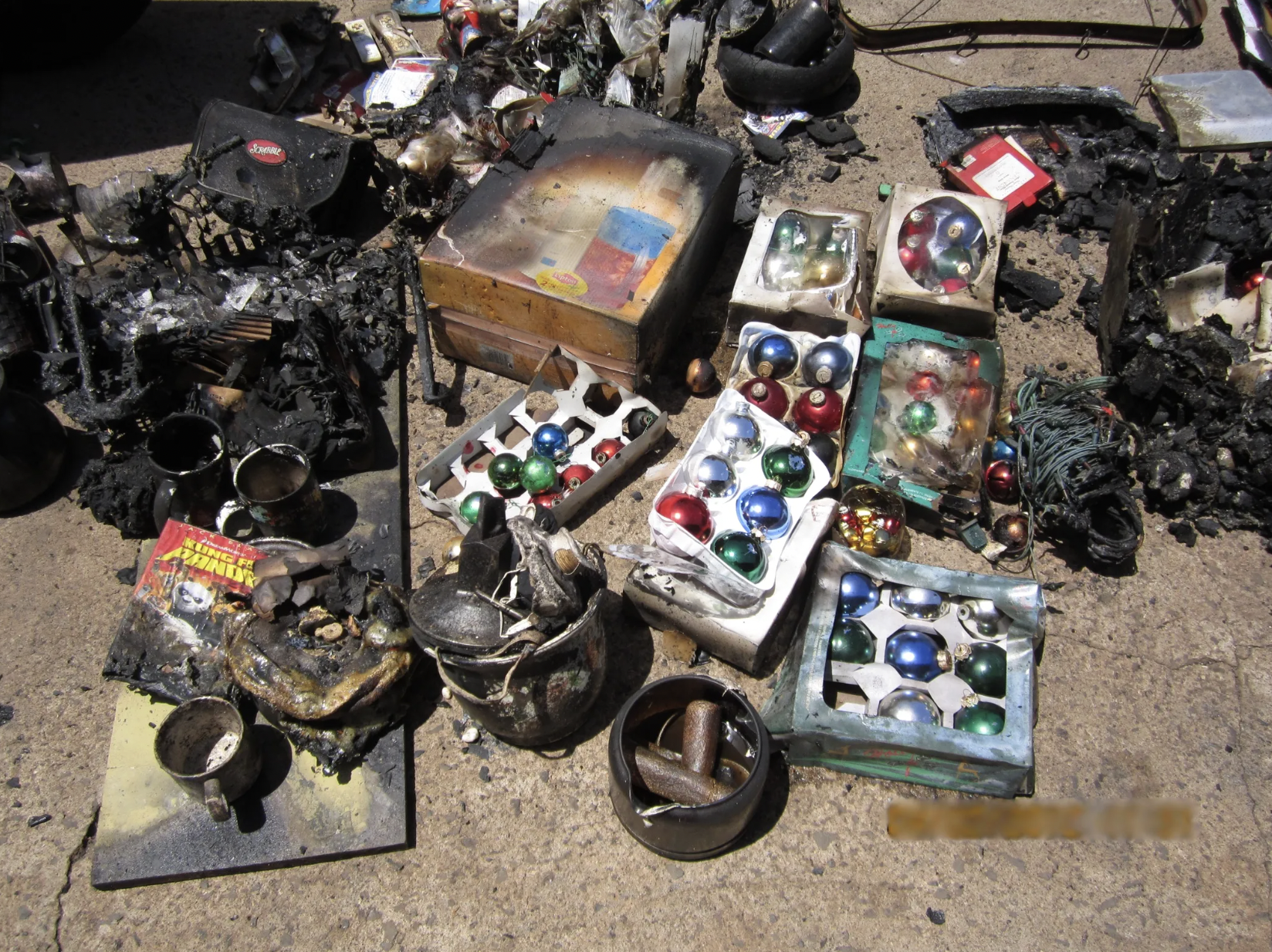 A collection of burnt and melted holiday ornaments, jewelry boxes, and decorative items laid out on the ground, with some resembling Christmas ornaments.