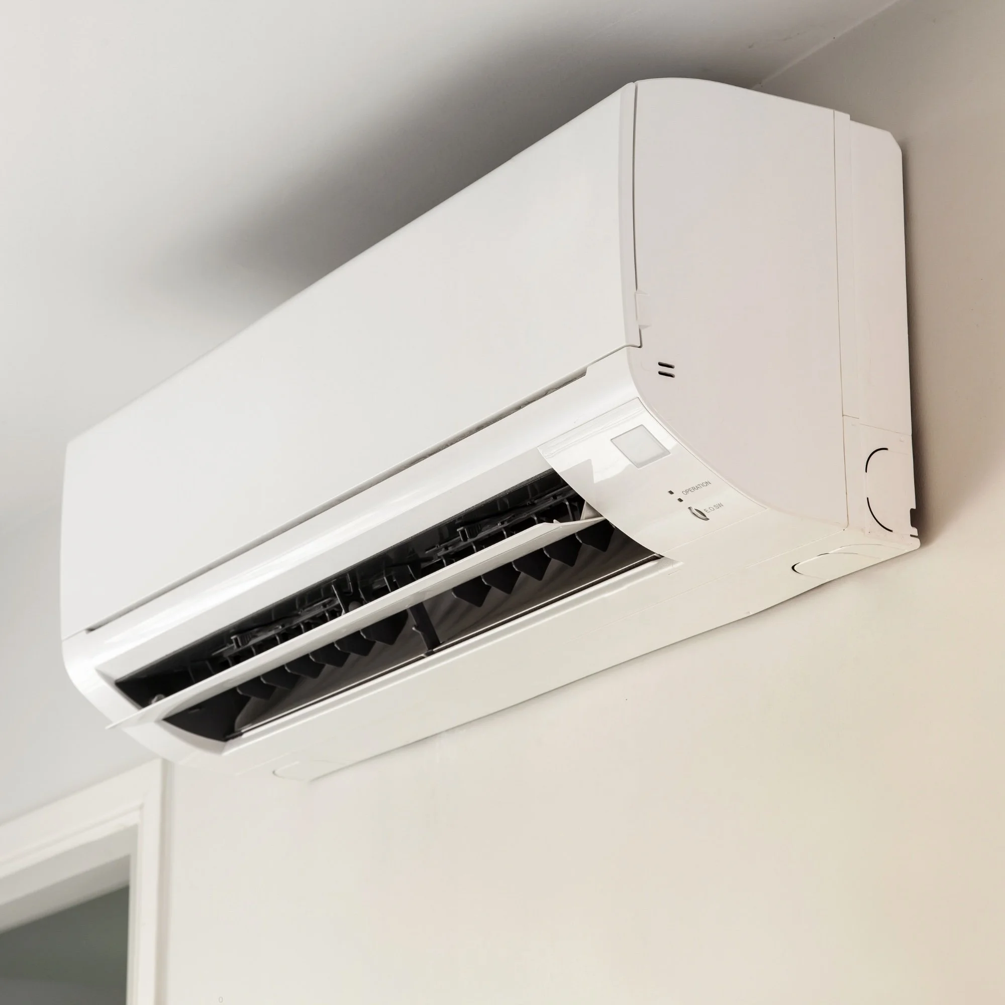 White wall-mounted air conditioning unit with black vents installed near the ceiling.