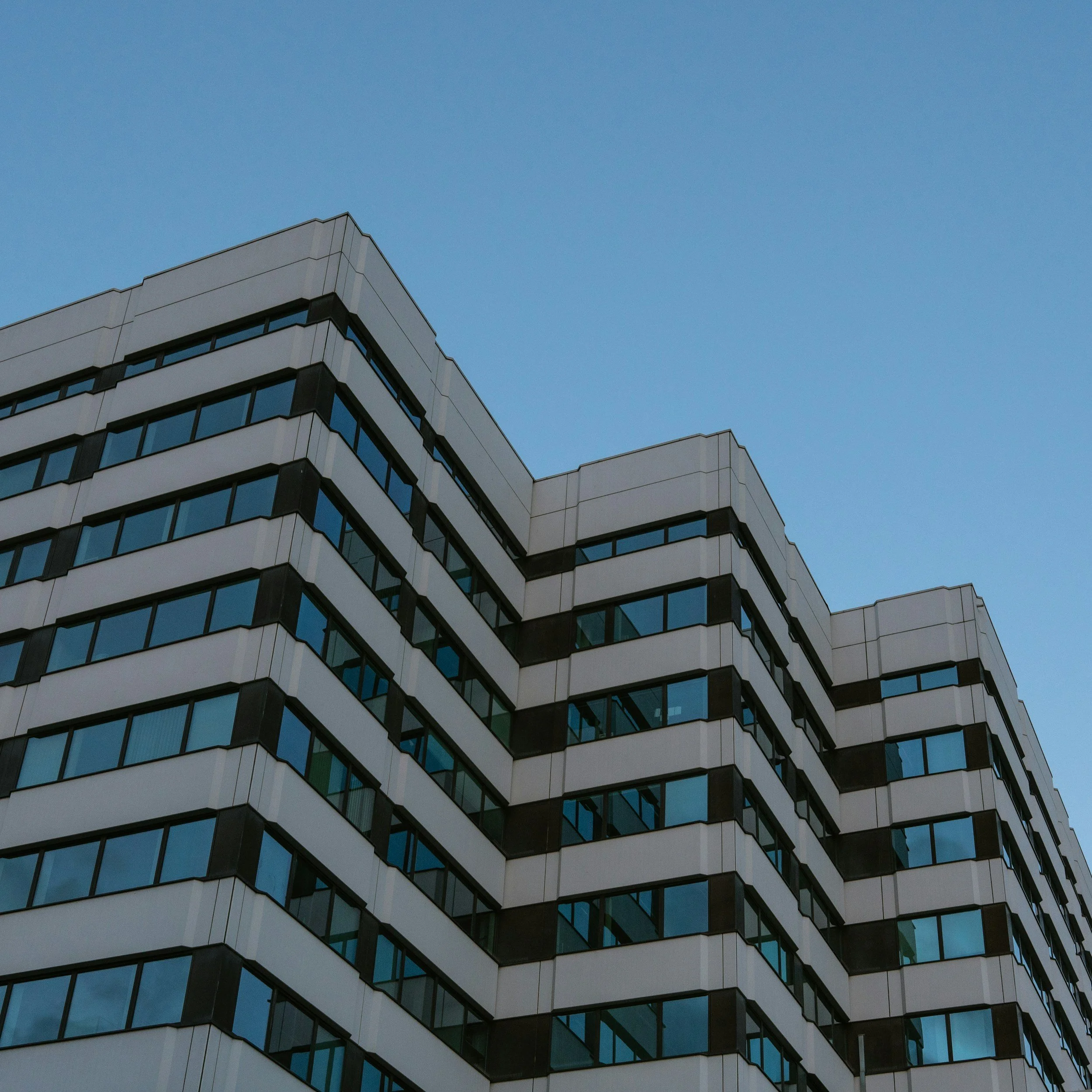 Modern multi-story building with glass windows and white exterior walls against a clear blue sky.