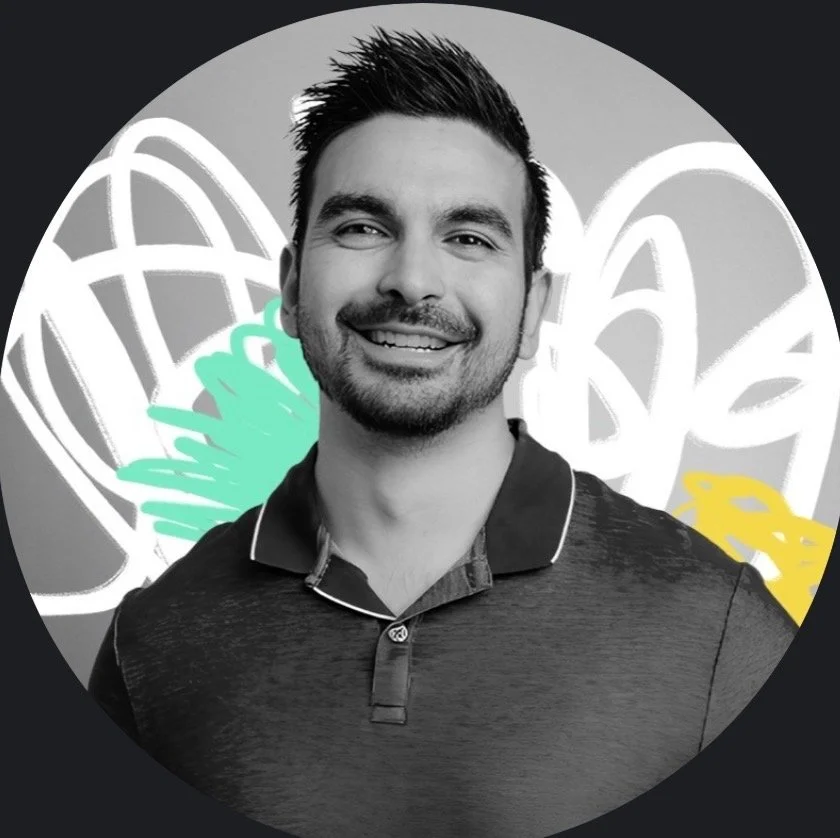 A smiling man with short dark hair, a beard, and a mustache, wearing a collared shirt, standing in front of a colorful, abstract background with white, light green, and yellow shapes.