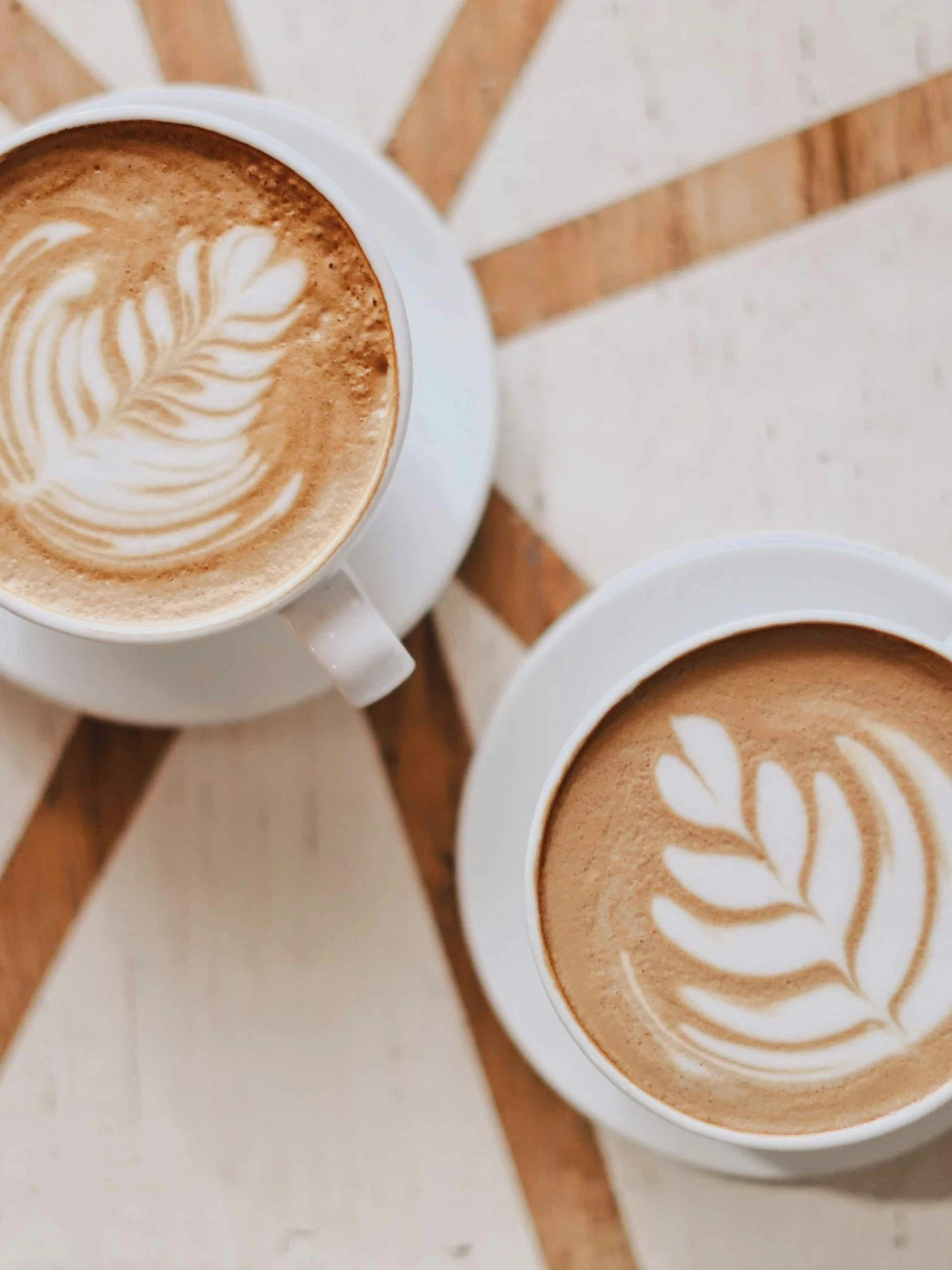 Two cups of coffee with latte art, placed on a wooden table.