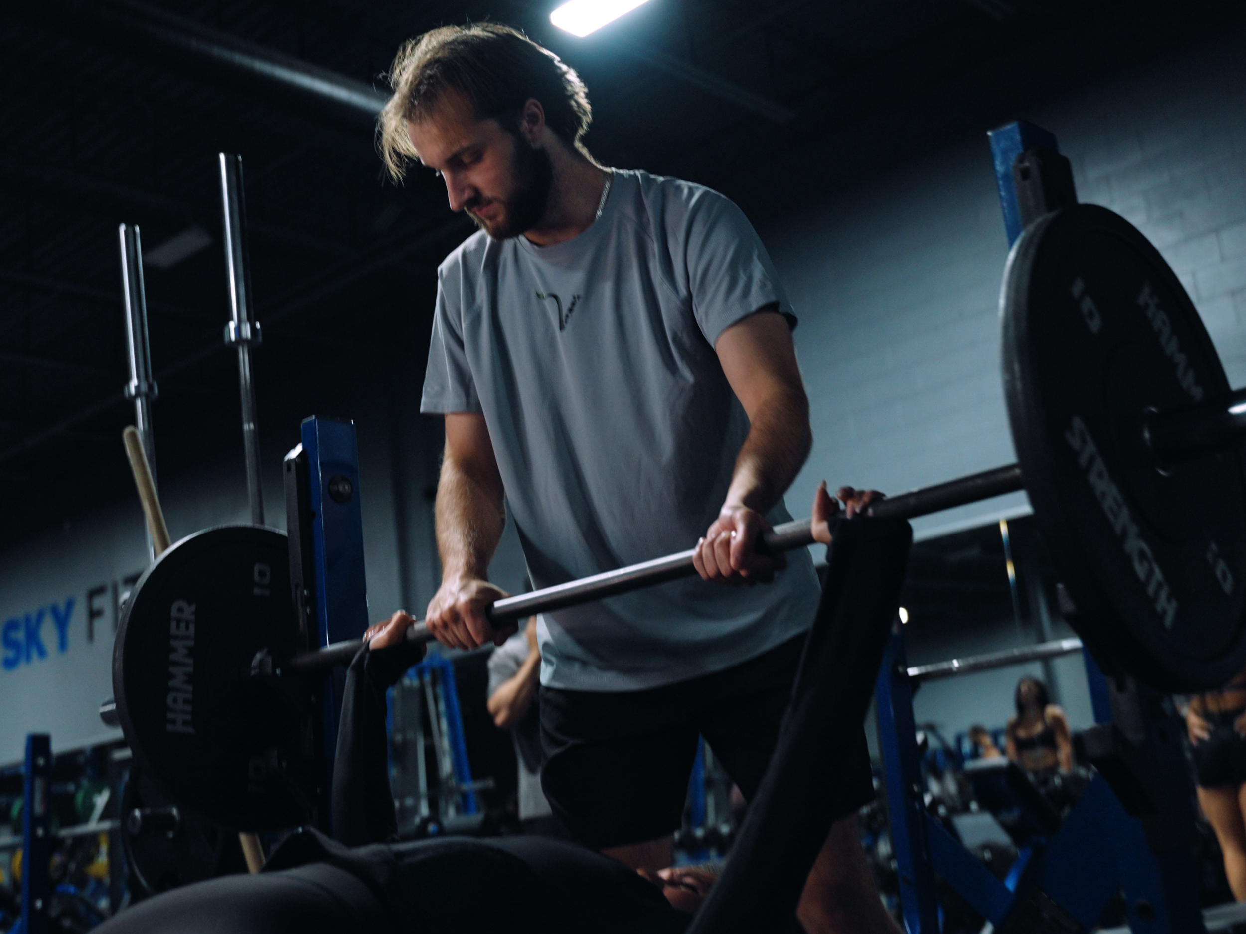 Young man lifting a barbell with weight plates in a gym, using proper form with a focused expression.