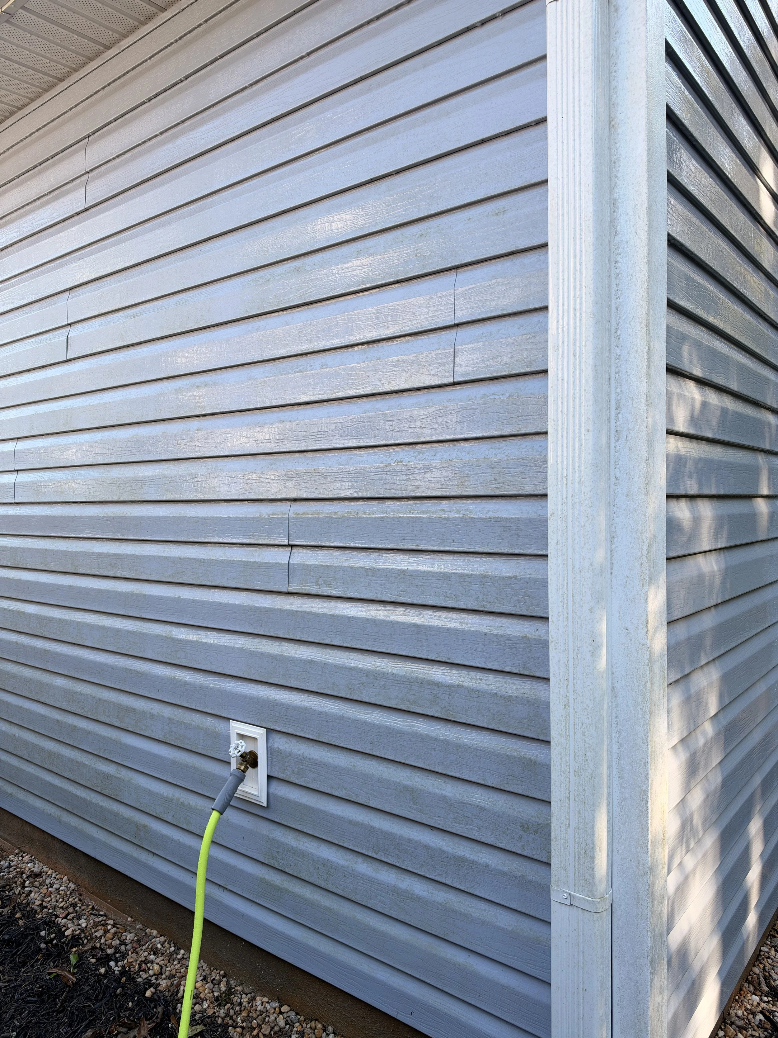 Blue-gray house siding with a garden hose connected to an outdoor faucet beside a downspout.