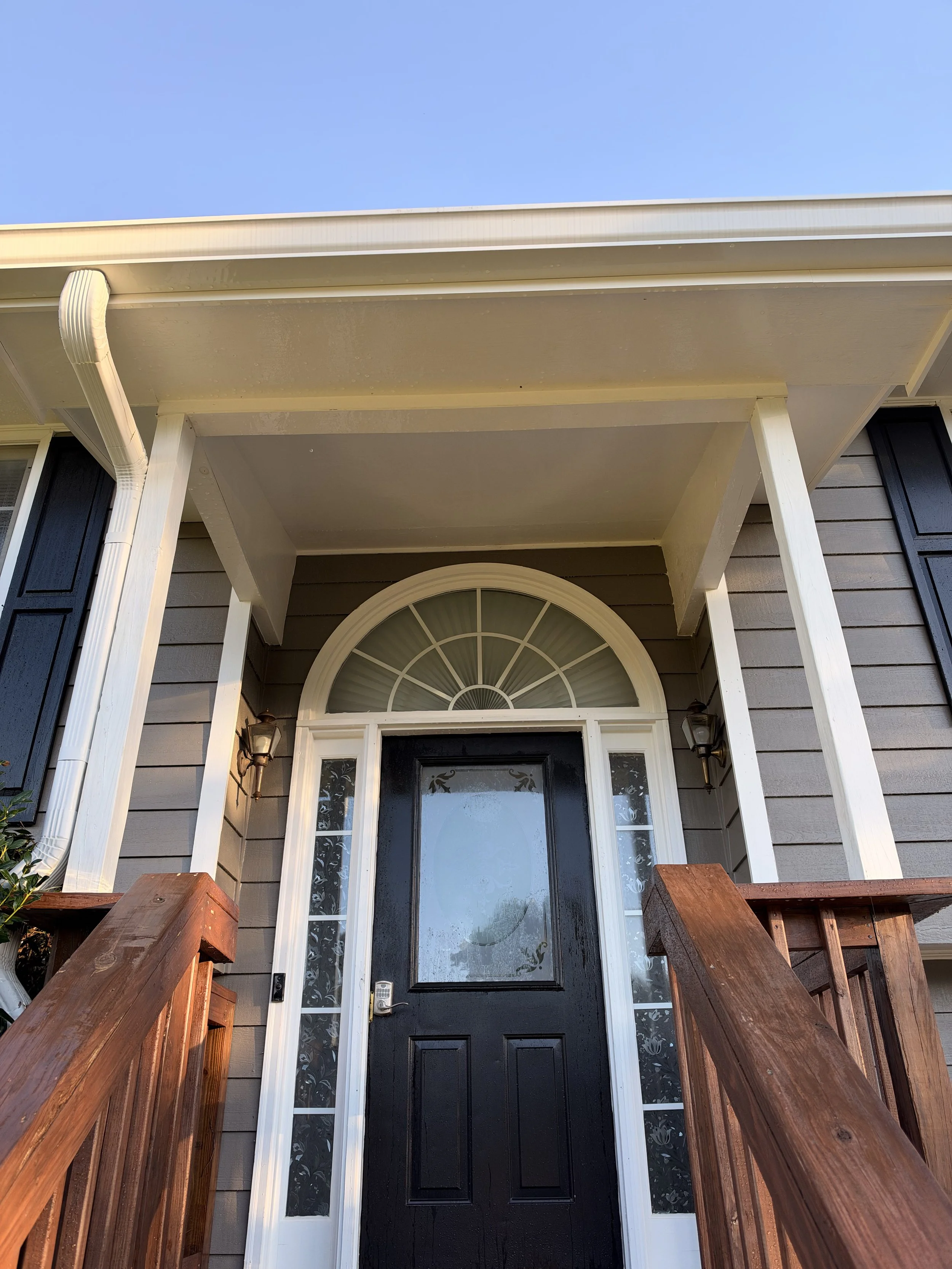 Front porch with a black entry door, white trim, sidelights, wooden railings, and covered roof.