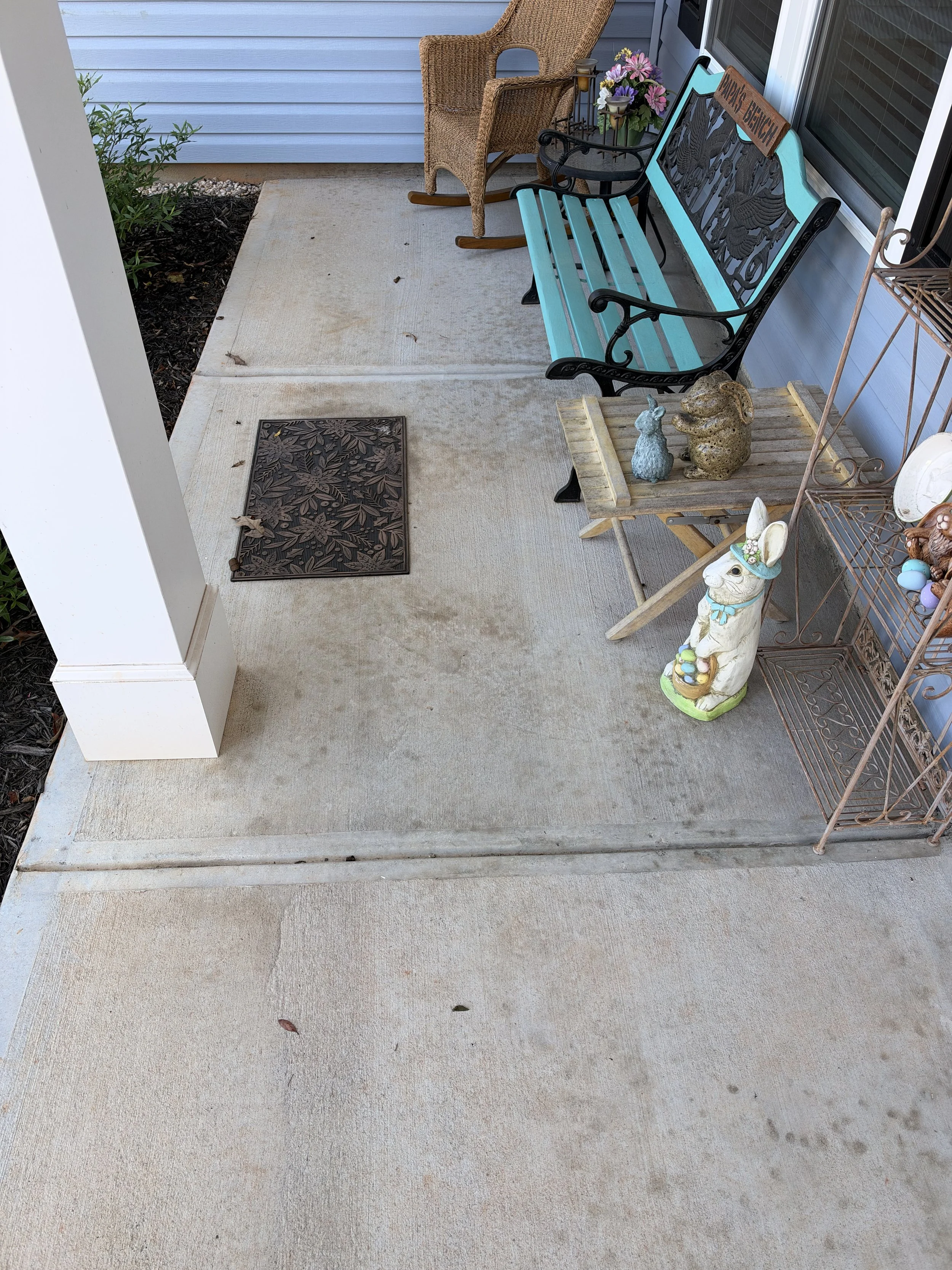 Decorated front porch with turquoise bench, wicker rocking chair, flowers, and rabbit garden statues