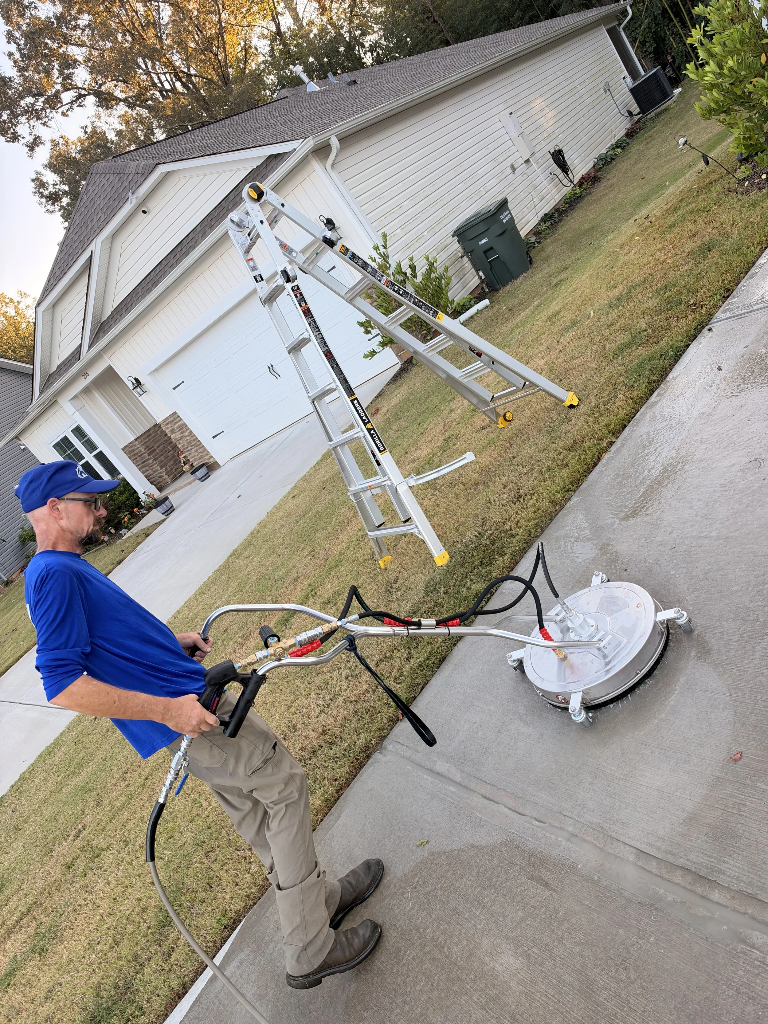 Technician pressure-washing a suburban home's exterior beside an extension ladder.