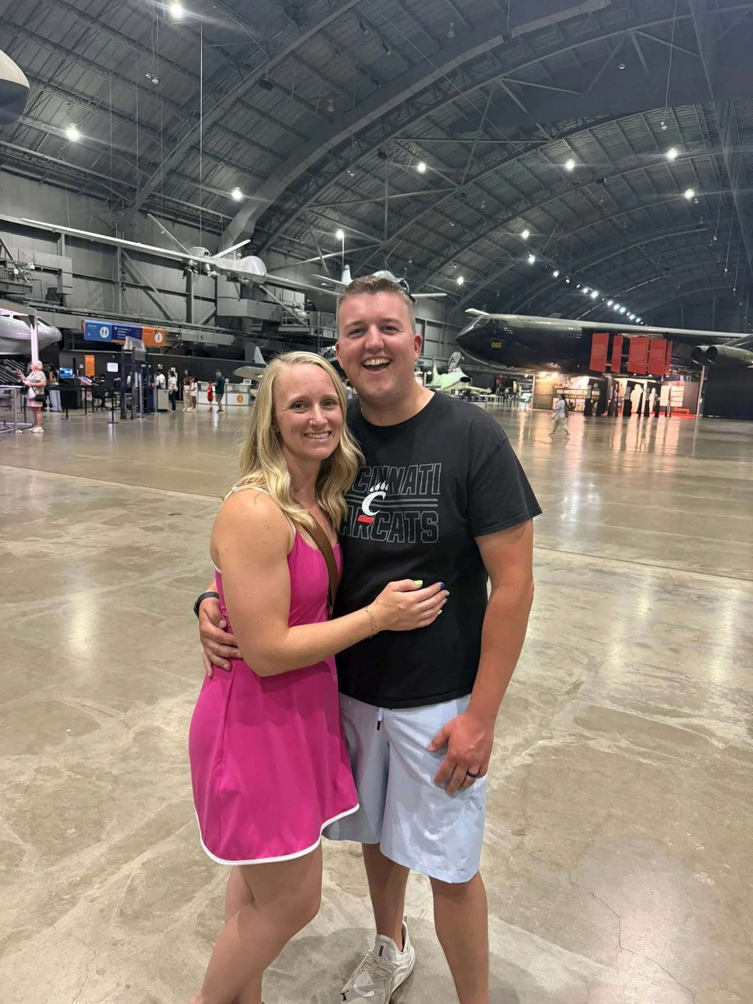 A smiling woman and man embrace each other in a museum in Dayton, Ohio with aircraft and helicopters in the background.