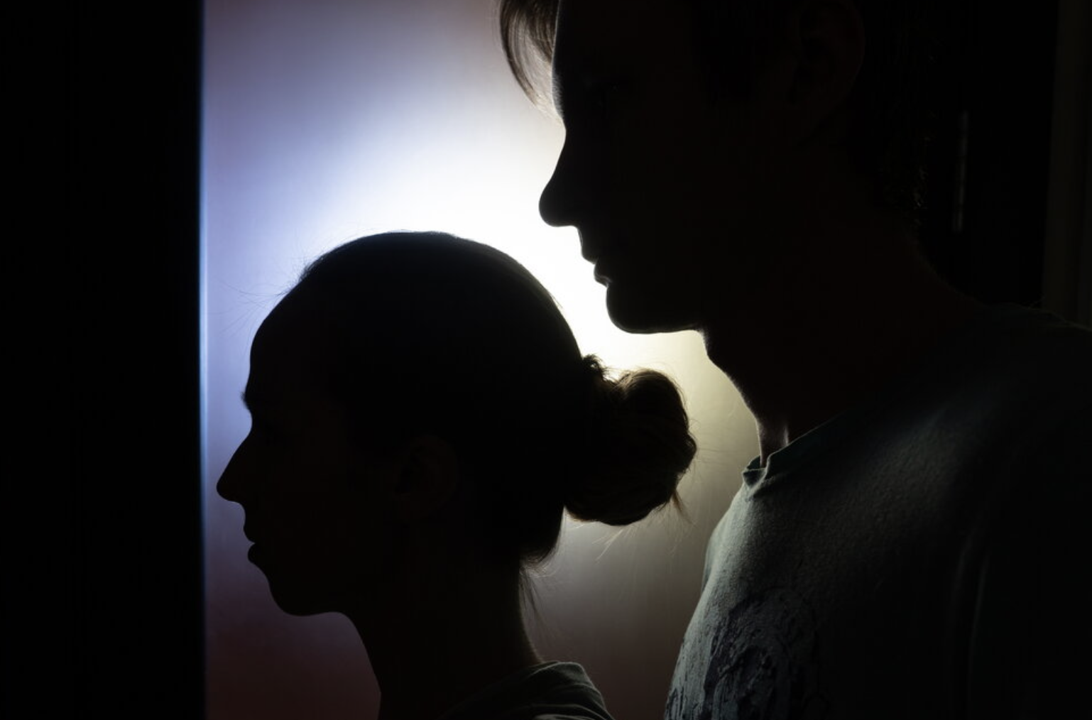 Silhouette of two women, one older and one younger, facing each other in profile, with a backlit background.