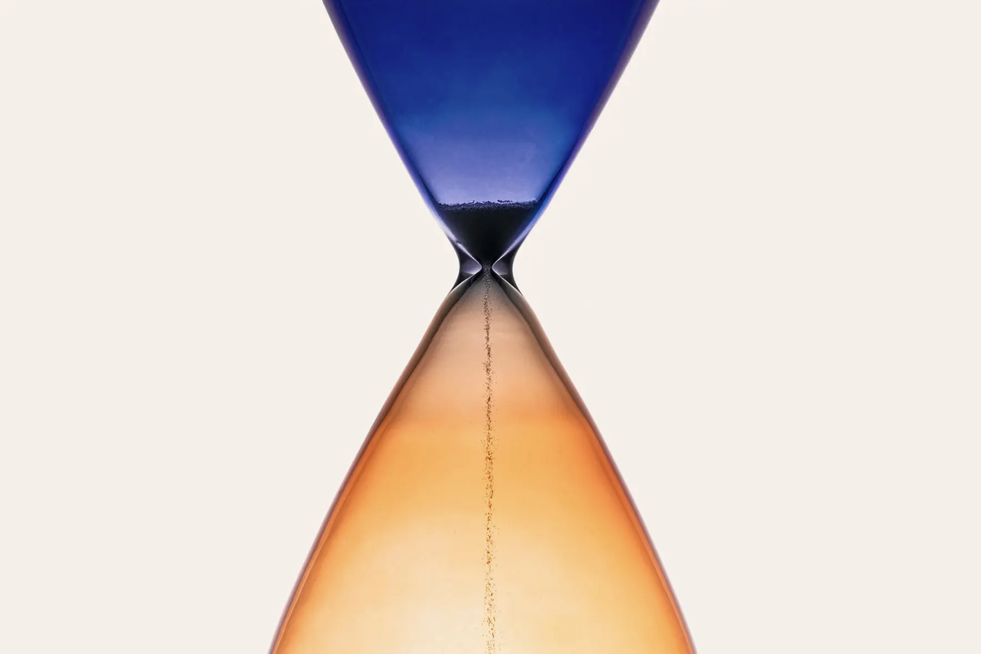 Close-up of an hourglass with blue sand in the upper chamber and orange sand in the lower chamber, with sand falling through the narrow middle.