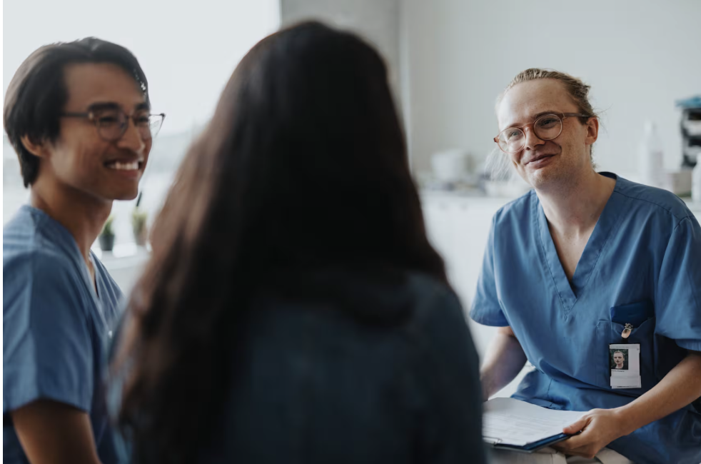 Three medical professionals in scrubs having a conversation with a patient in a medical office or clinic.