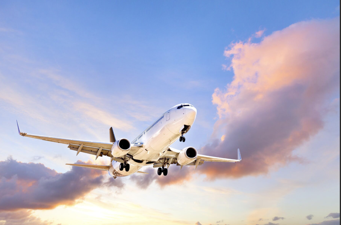 A white commercial airplane flying in the sky at sunset with pink and purple clouds.