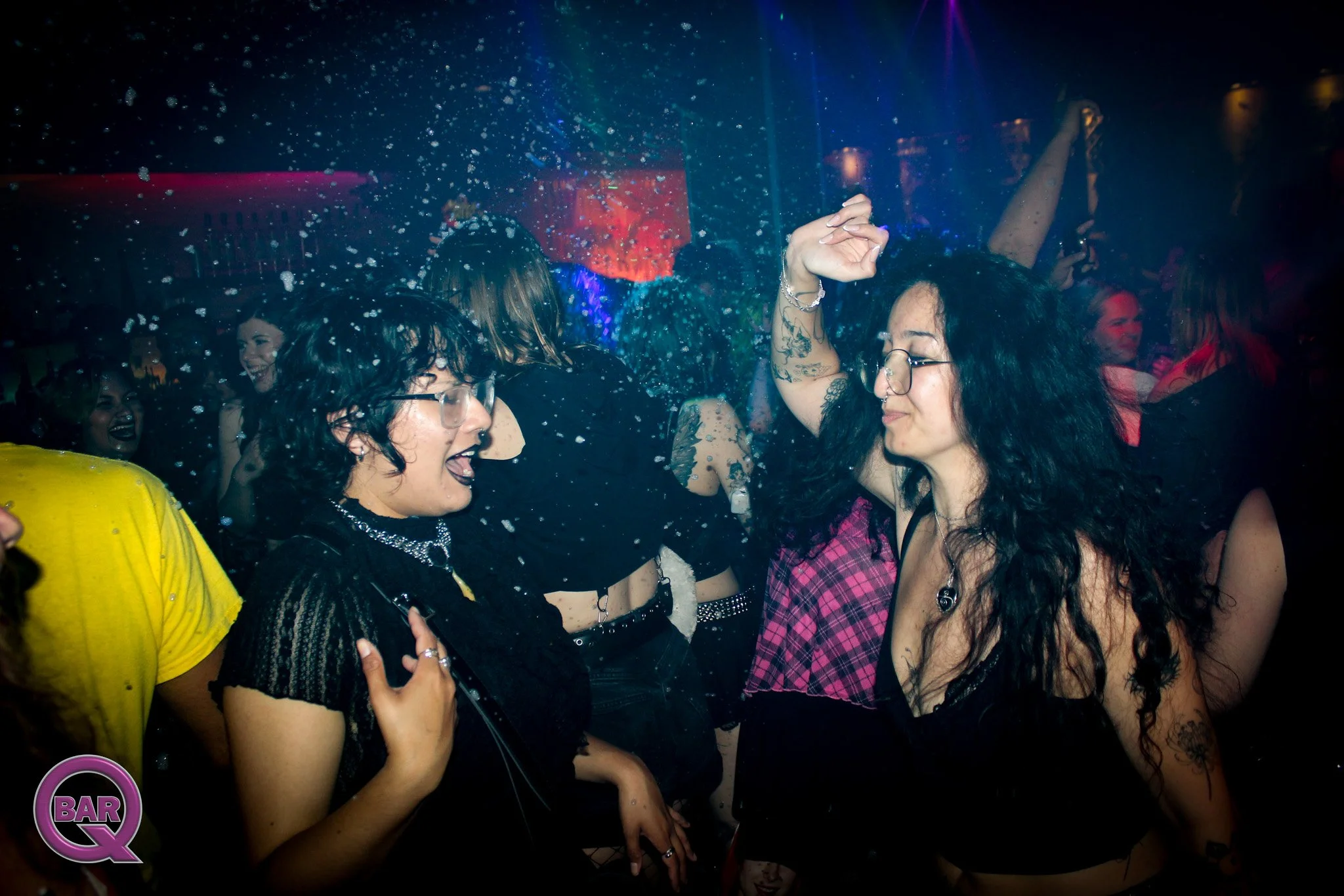 People dancing and smiling in a dark nightclub with colorful lights and water splashing around.
