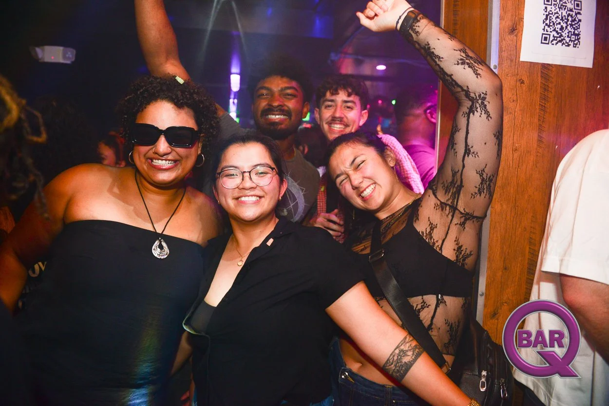 Group of five diverse friends smiling and celebrating at a bar or nightclub, with colorful lighting and a QR code on the wall.