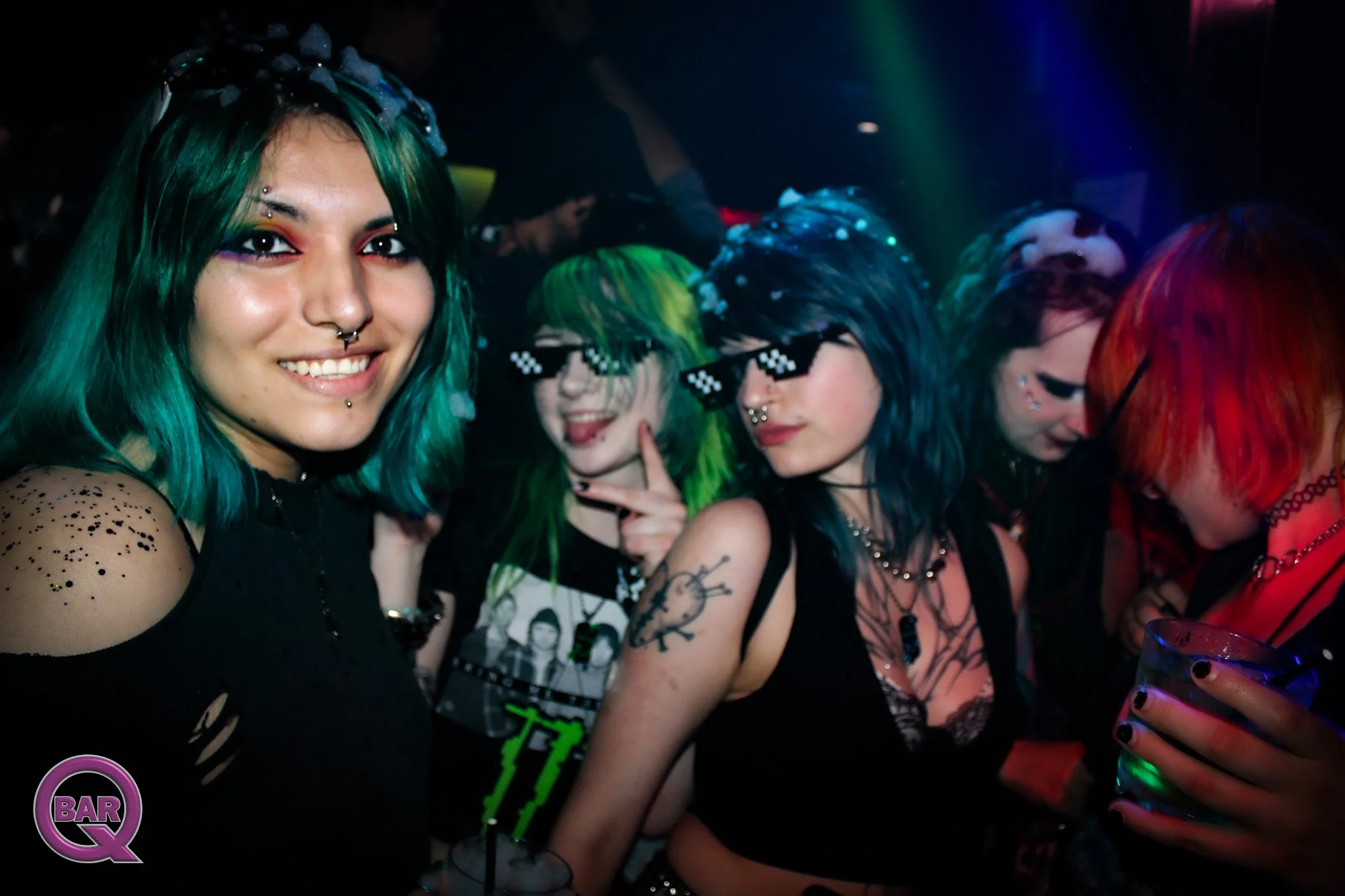 A group of young women with brightly colored hair at a nightclub, smiling and enjoying the party.