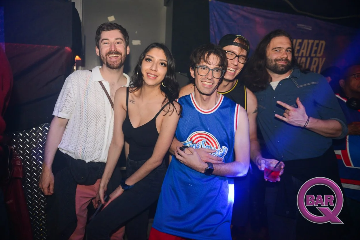 Group of five friends at a party, some wearing casual outfits and one in a basketball jersey, smiling and posing for the camera, with a bar logo in the corner.