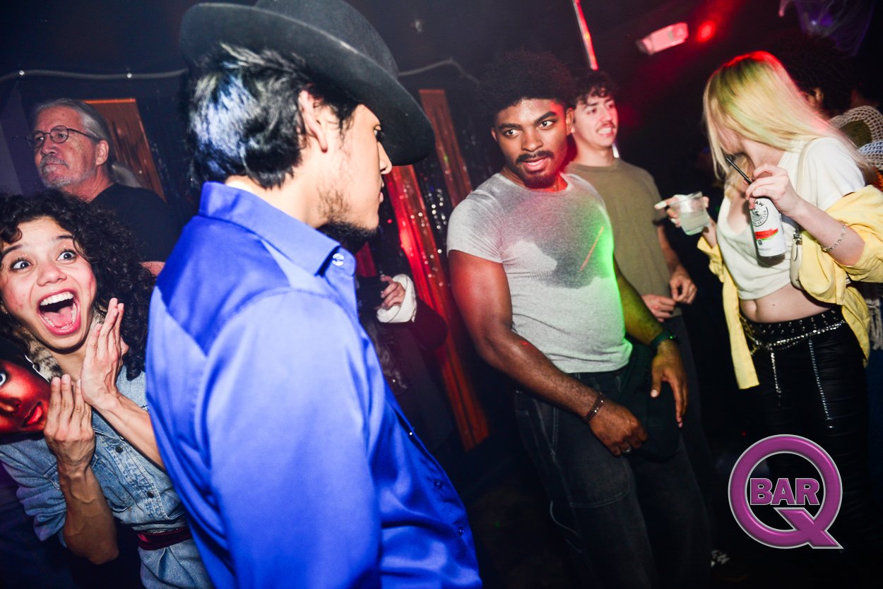 Group of diverse young adults dancing and socializing in a nightclub, with colorful lights and a 'Bar Q' logo in the corner.