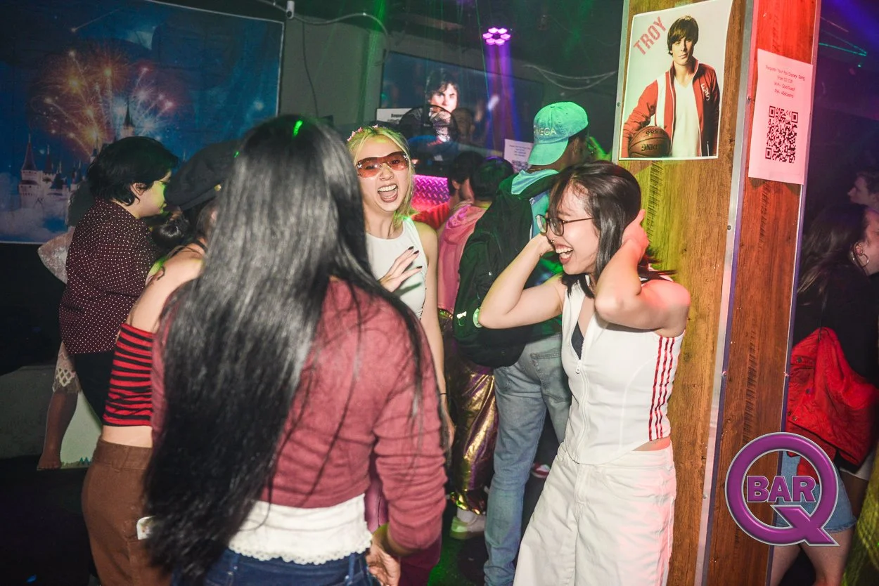 A group of young people enjoying themselves at a party or nightclub, dancing and laughing together in colorful lighting.