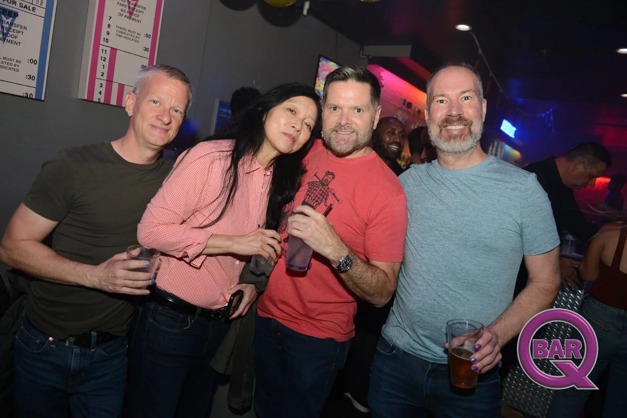 Four friends posing with drinks in a bar, smiling and enjoying nightlife.