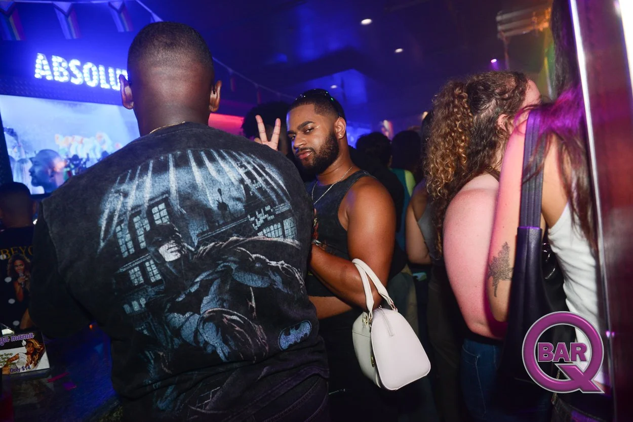 People socializing in a nightclub with colorful lighting and a sign that says 'ABSOLUT' in the background.