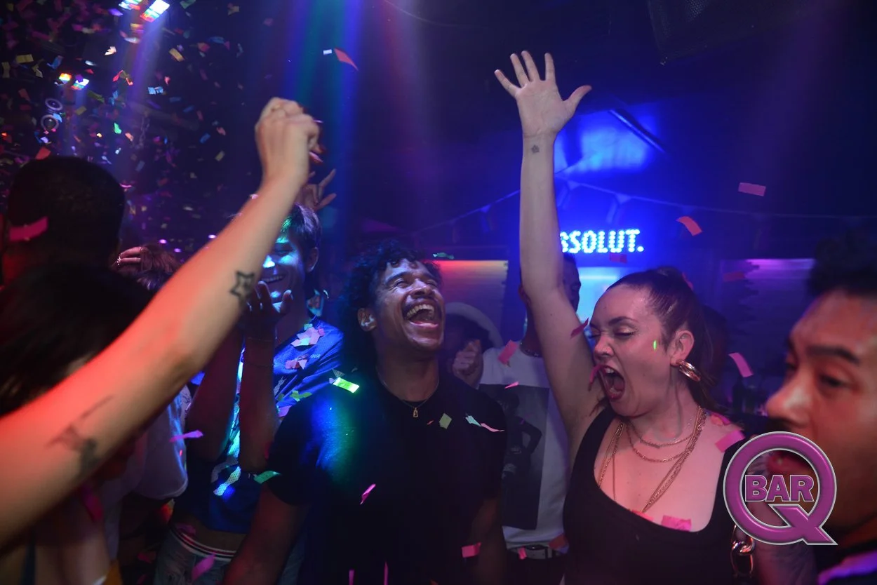 People dancing and celebrating in a nightclub with colorful confetti and flashing lights.
