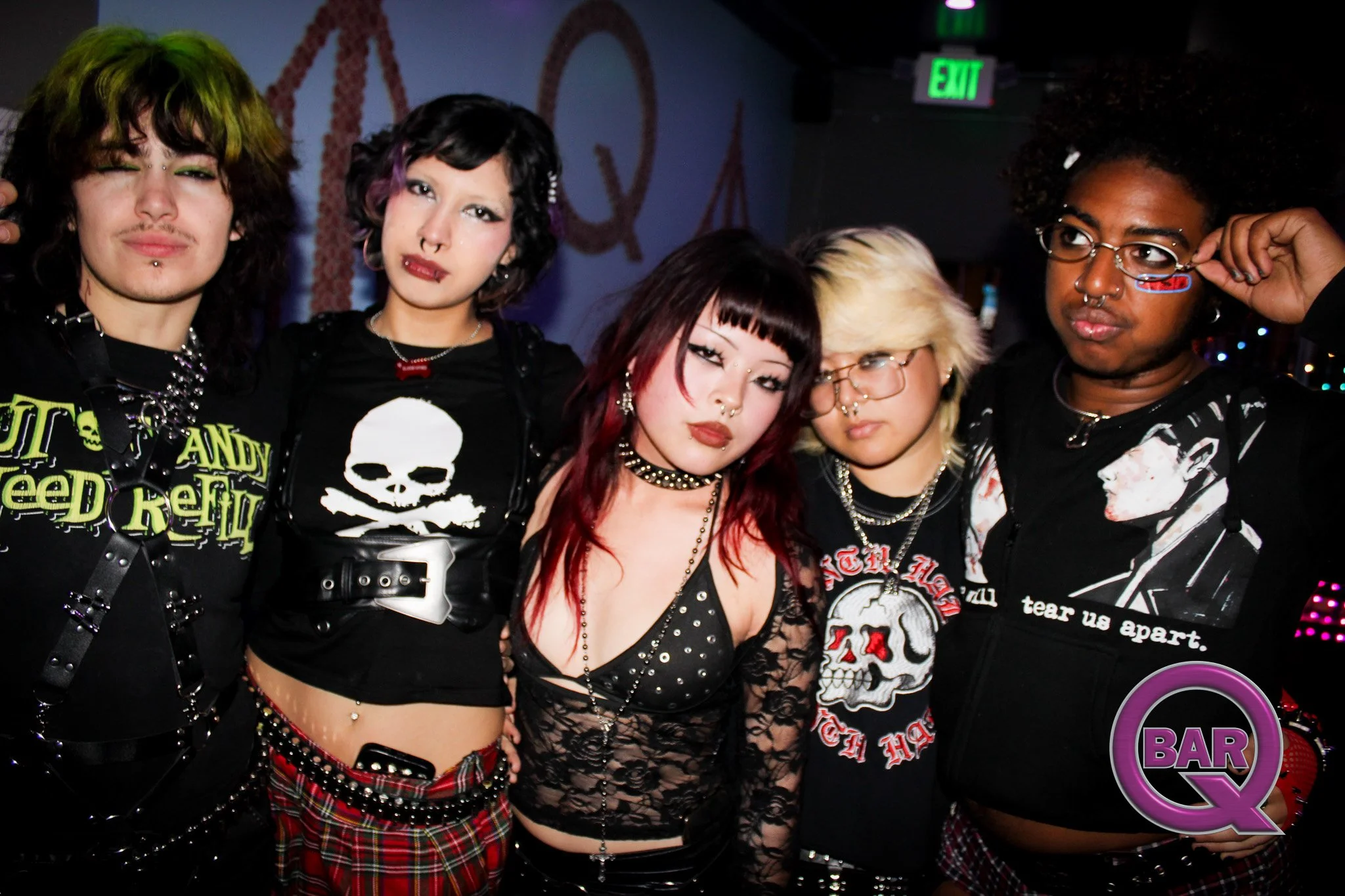 Group of five young adults dressed in alternative fashion, standing together in a bar or nightclub.