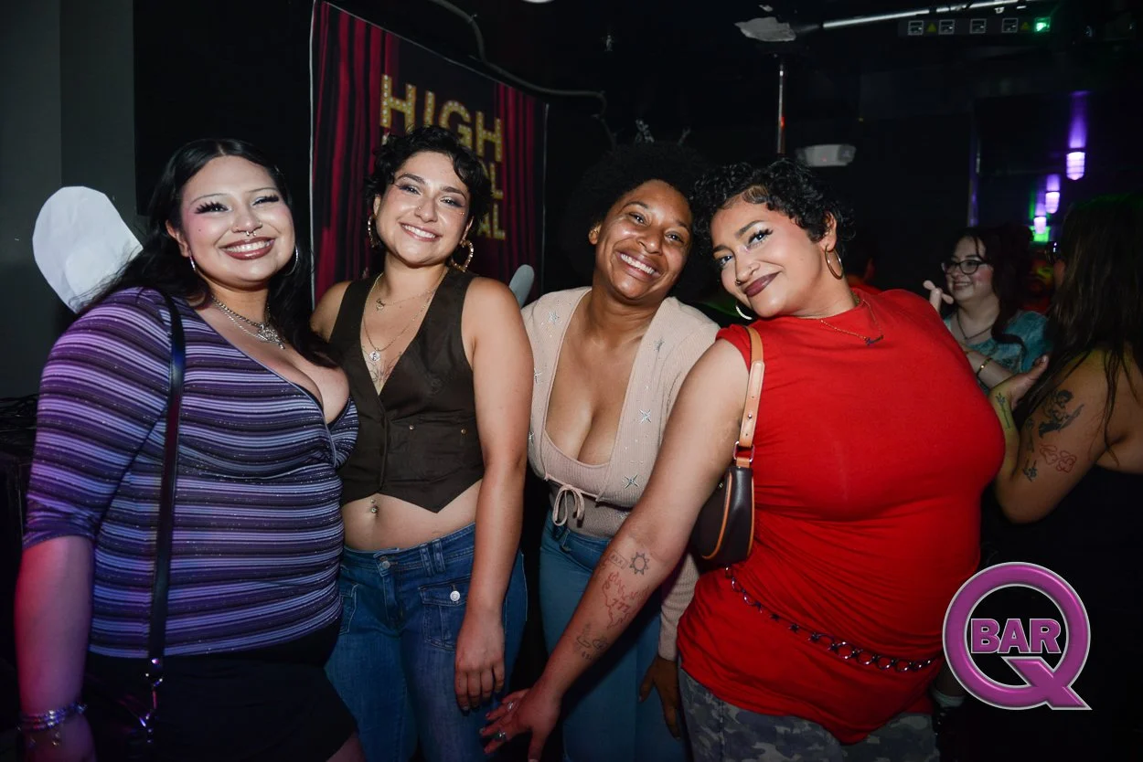 Group of four women smiling at a nightclub, with colorful lights and a 'High' sign in the background, some with visible tattoos and jewelry.
