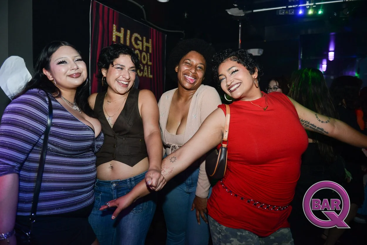 Four women smiling and holding hands at a nightclub or bar, with a sign reading 'High School Musical' and a logo 'BAR Q' visible in the background.