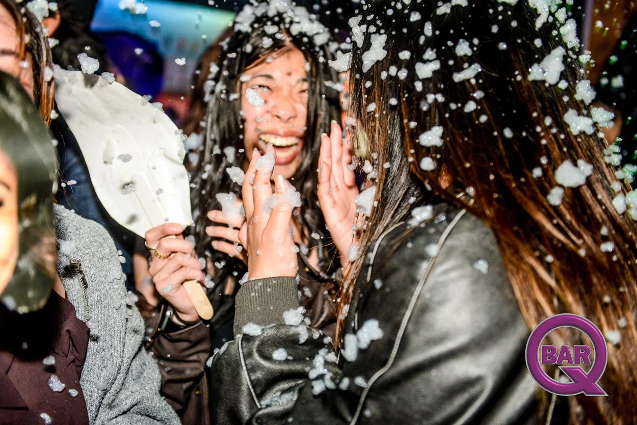 Group of women celebrating at a foam party, with foam on their hair and clothes, having fun and smiling.