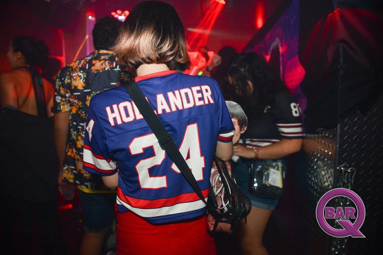 Person wearing a New York Rangers hockey jersey with the name 'Holland' and number 24, at a crowded nightclub with red lighting.