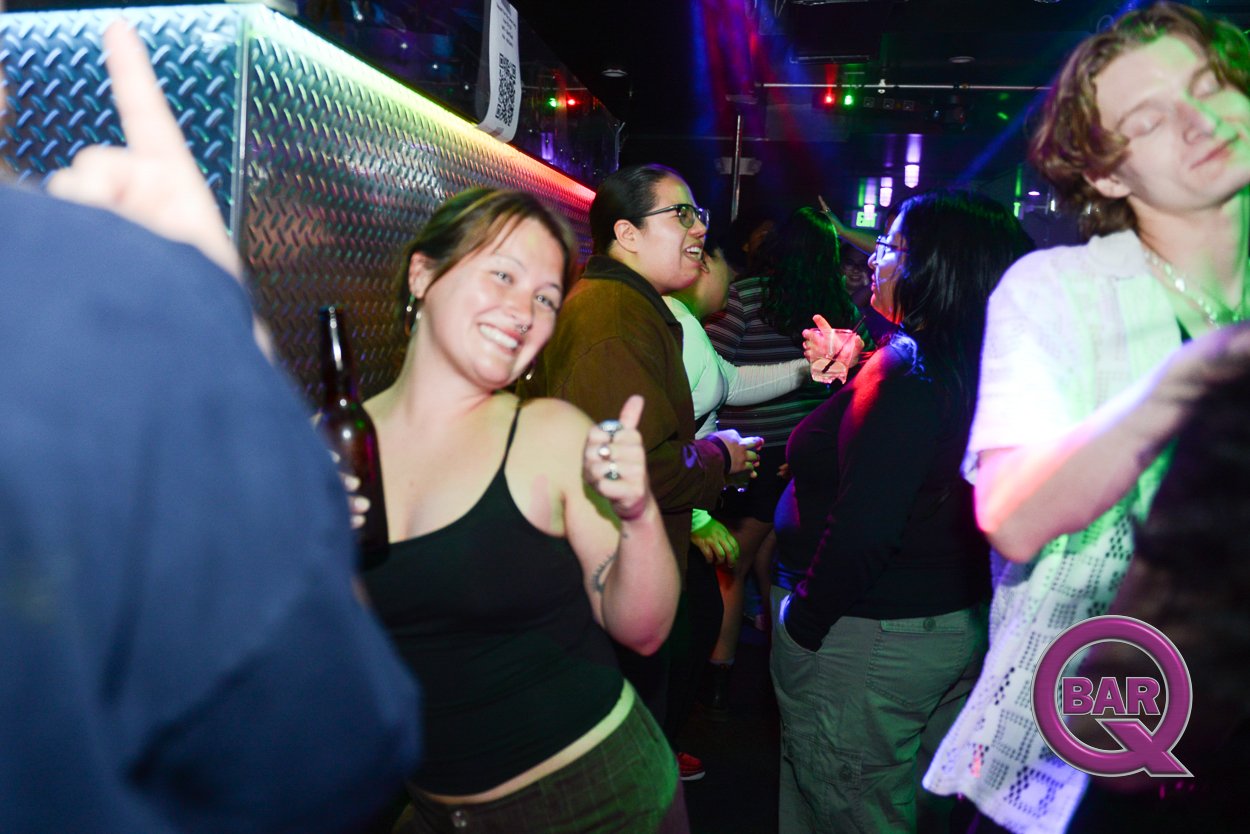 People dancing and socializing at a nightclub or bar, with neon lights and a vibrant atmosphere.