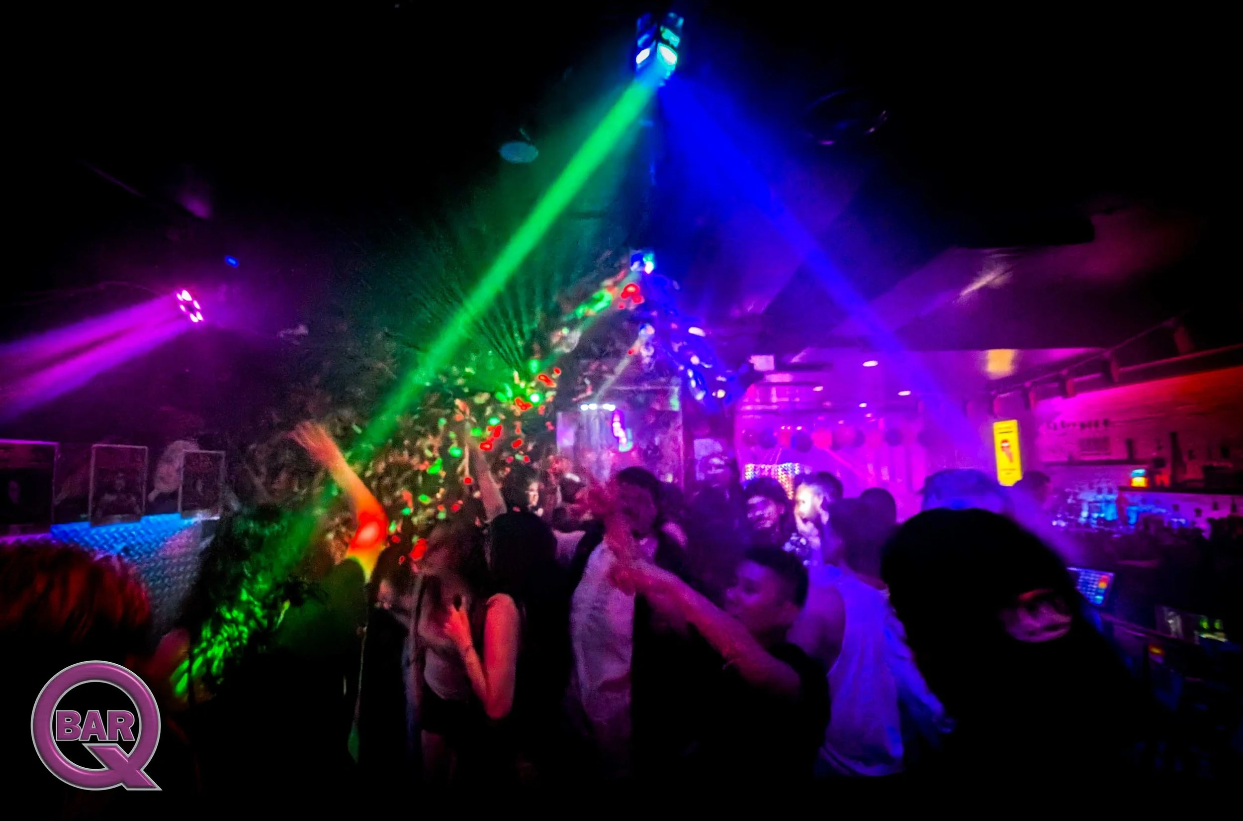 A crowded nightclub with colorful laser lights and people dancing and socializing.