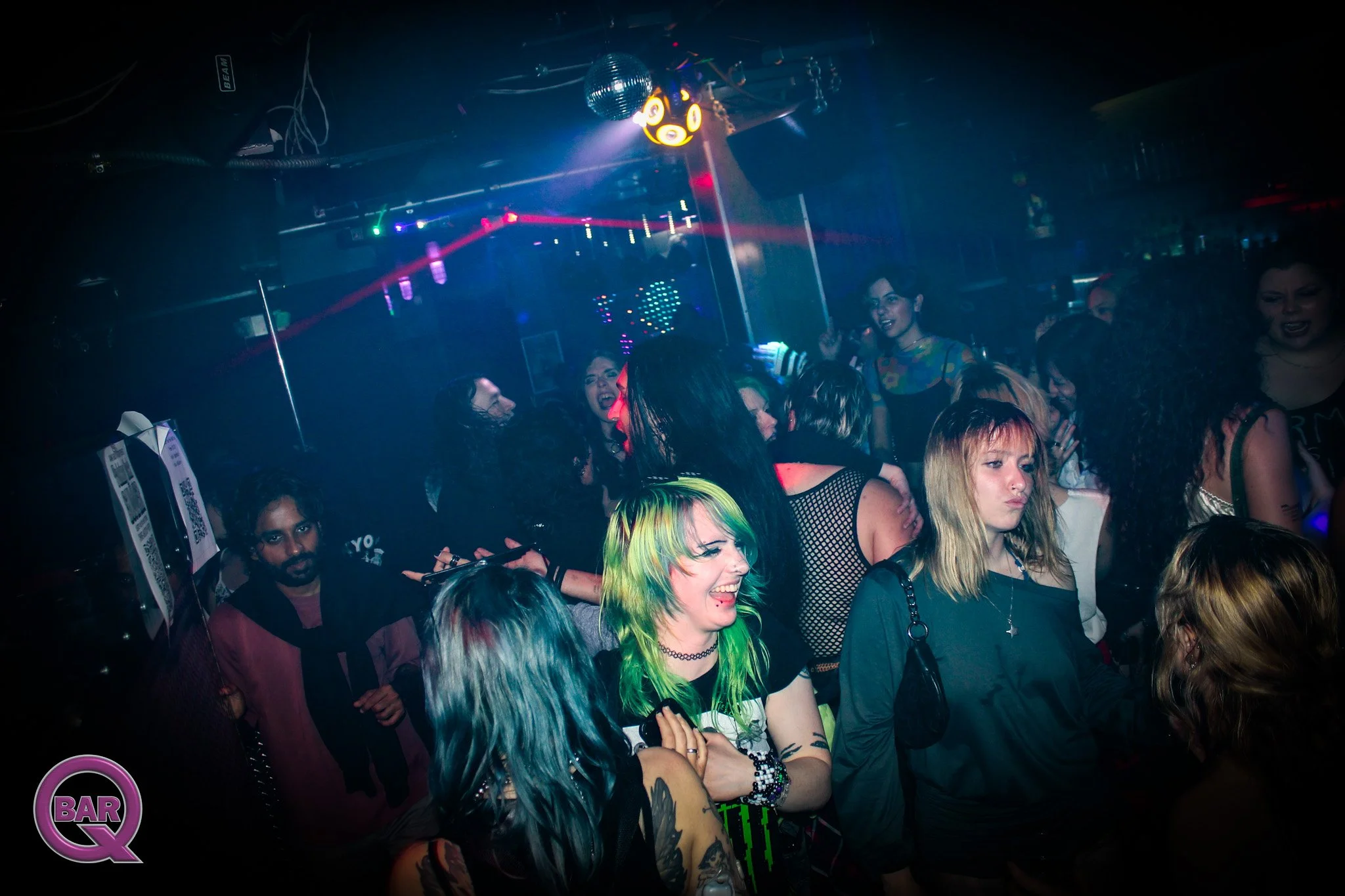 Crowd of people dancing and enjoying music in a nightclub with colorful laser lights and a disco ball overhead.