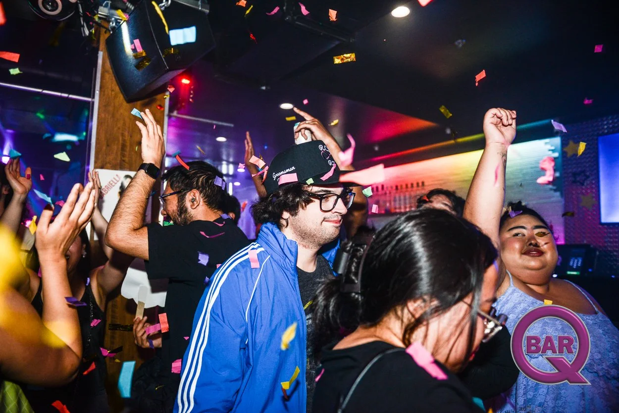 People dancing and celebrating in a nightclub with colorful confetti falling from above, and bright lights illuminating the scene.
