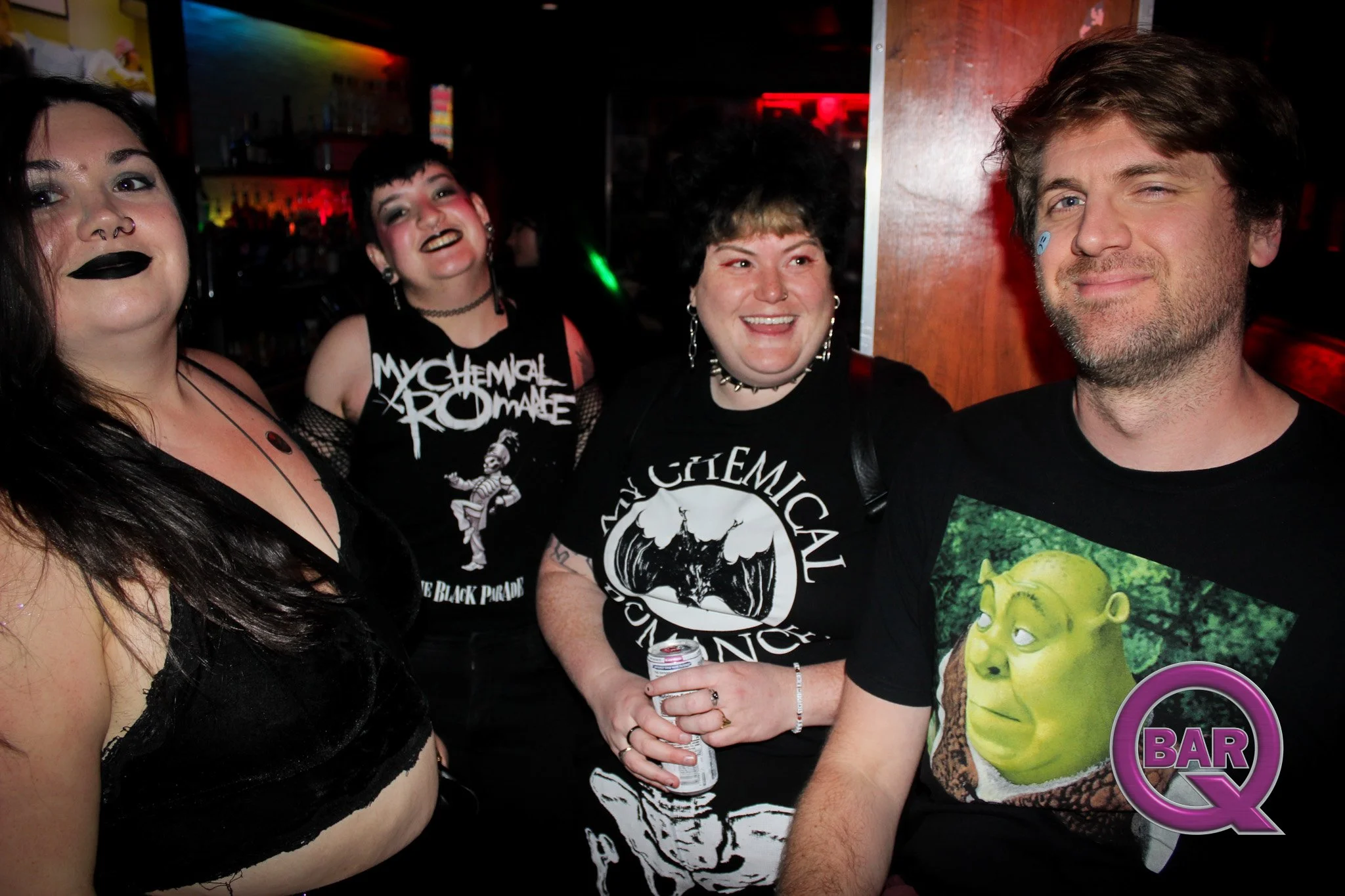 Group of four friends at a bar, smiling and enjoying themselves, with dark background and colorful lighting.