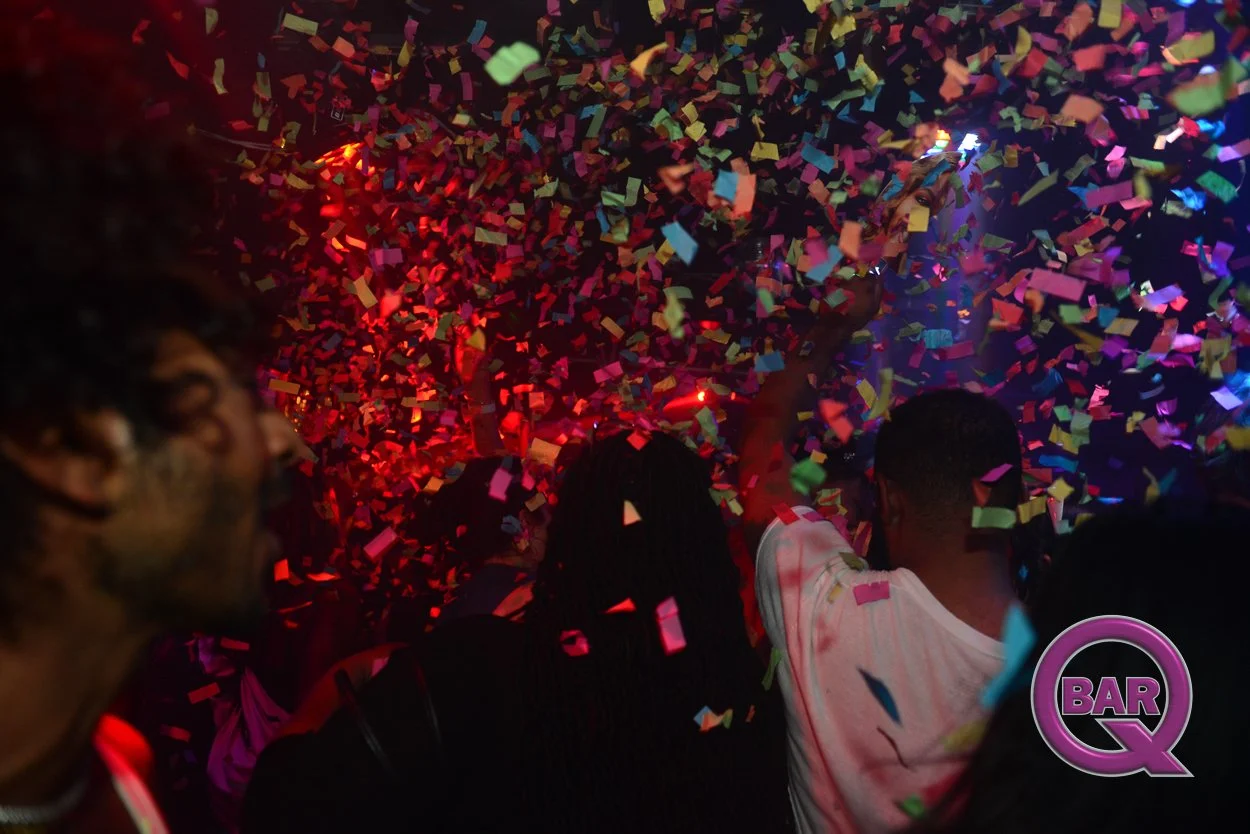 People dancing in a nightclub with colorful confetti falling from the ceiling and a purple BAR Q logo in the corner.