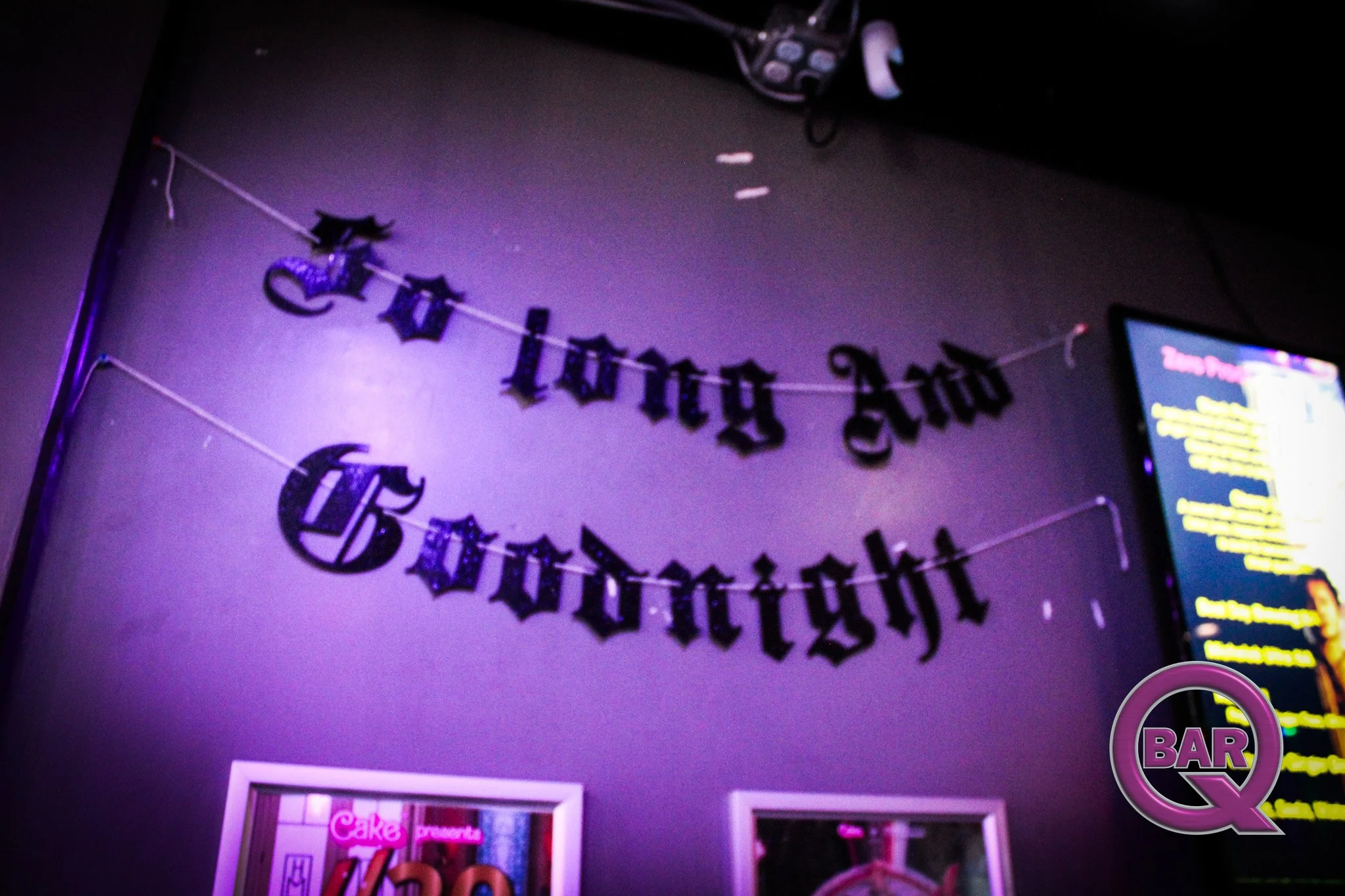 Decorations on a wall that say 'Happy Birthday' in black gothic-style letters, with a purple glow lighting the scene.