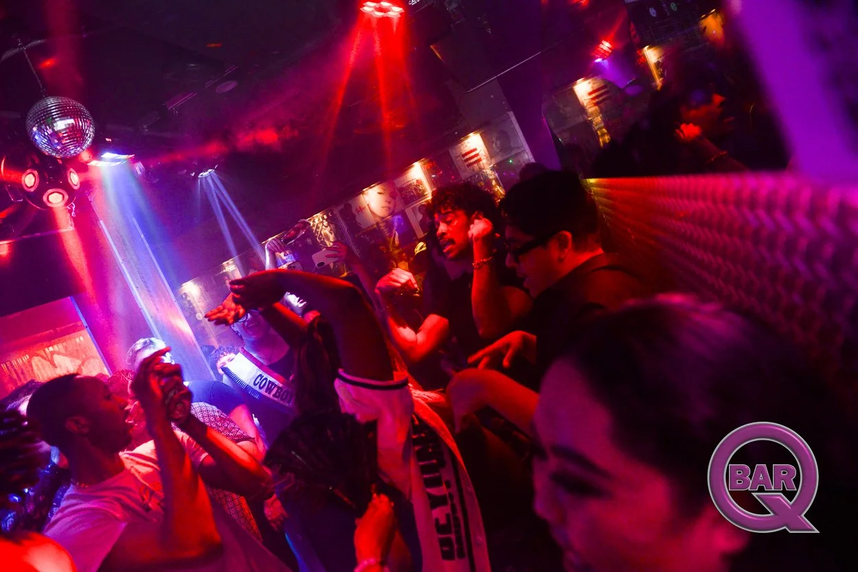 People dancing and socializing at a nightclub with colorful lights and a disco ball.