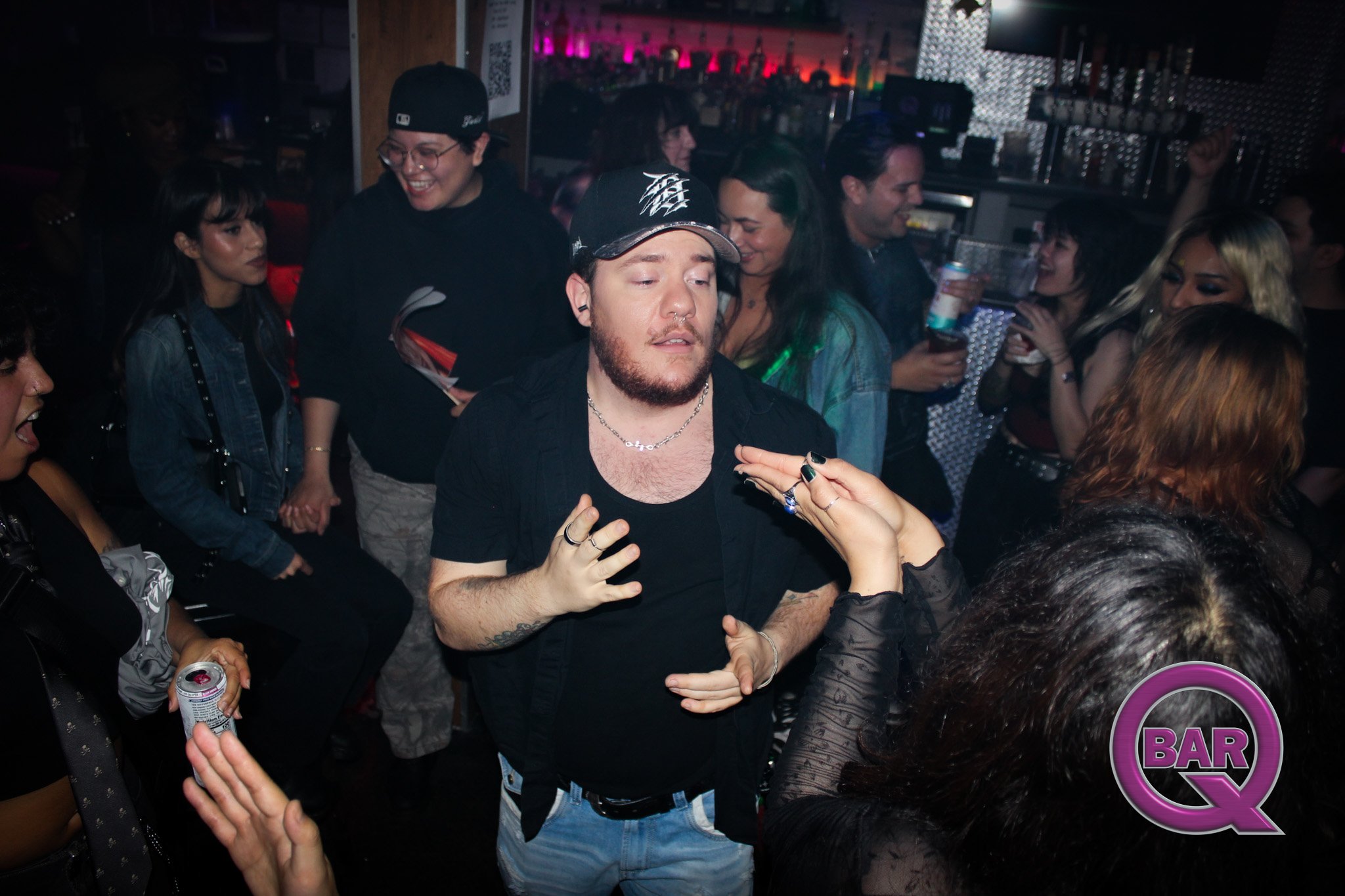 A group of people dancing and socializing at a bar or nightclub, with colorful lighting and a crowded atmosphere.