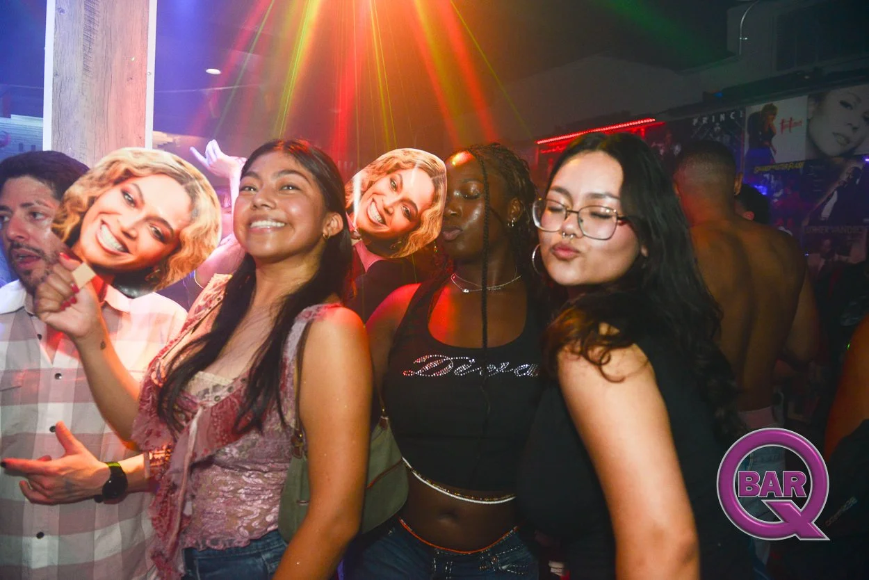 Group of people at a party or nightclub, some wearing masks with smiling faces, colorful lighting, and a 'Bar Q' logo in the corner.