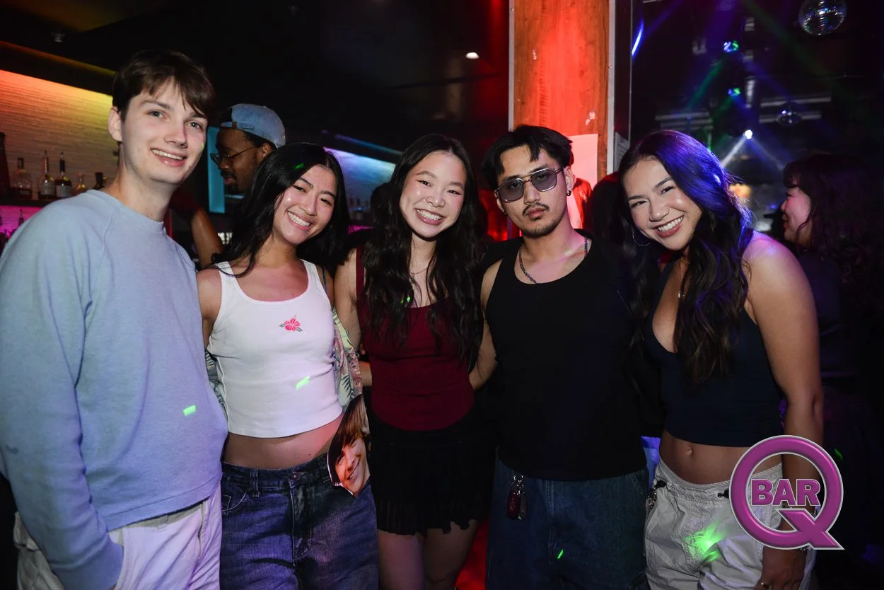 A group of five young adults posing together in a nightclub with colorful lighting, smiling and enjoying the night.