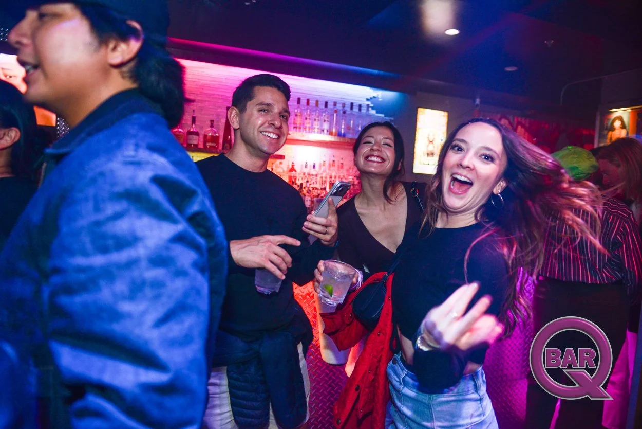 Group of young adults at a bar enjoying drinks and having fun with colorful lighting and a bar in the background.