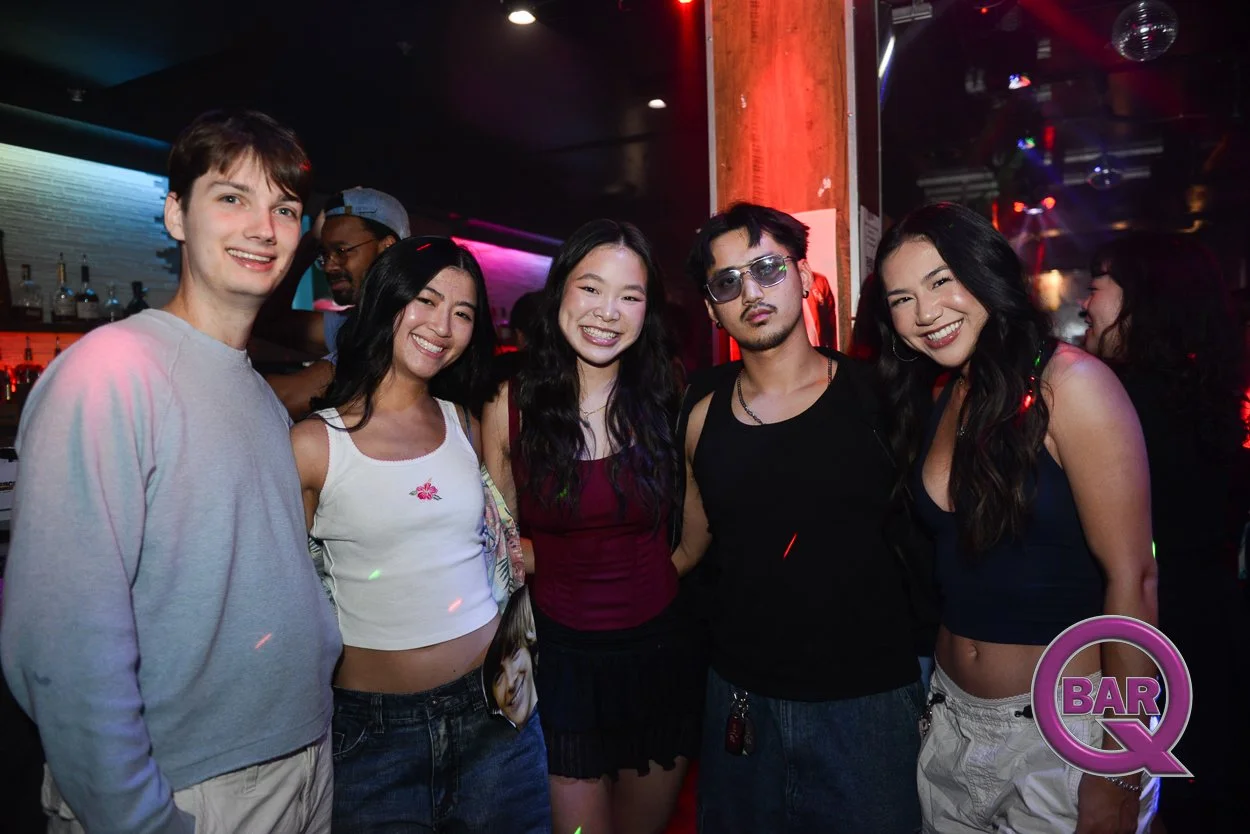 Group of five young adults smiling at a nightclub or bar. They are standing together with colorful lights and music equipment in the background. One person is wearing sunglasses, and another has a small bag. There is a BAR Q logo in the bottom right 