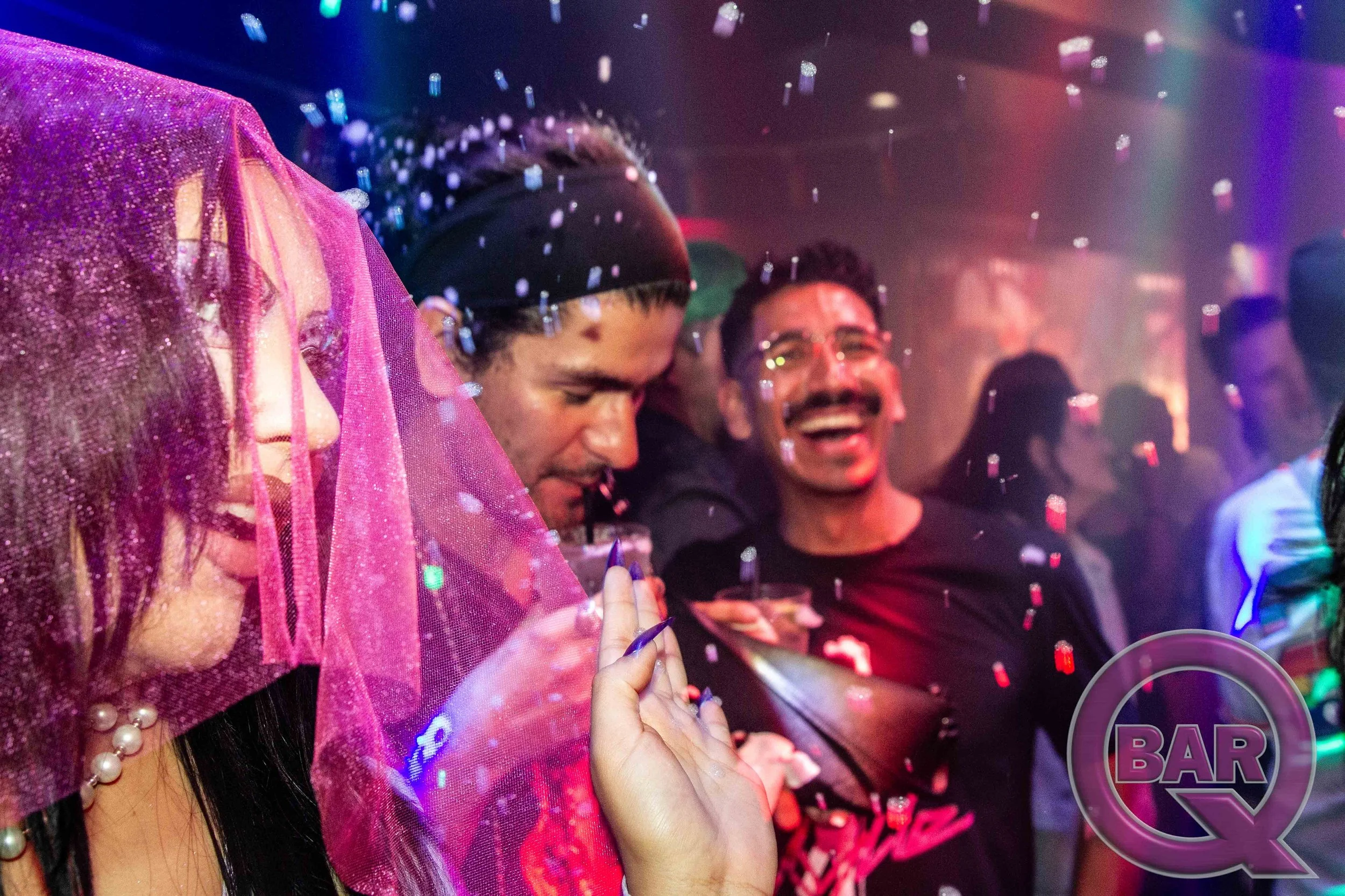 People celebrating in a lively bar or club with confetti falling, colorful lighting, and smiling faces.