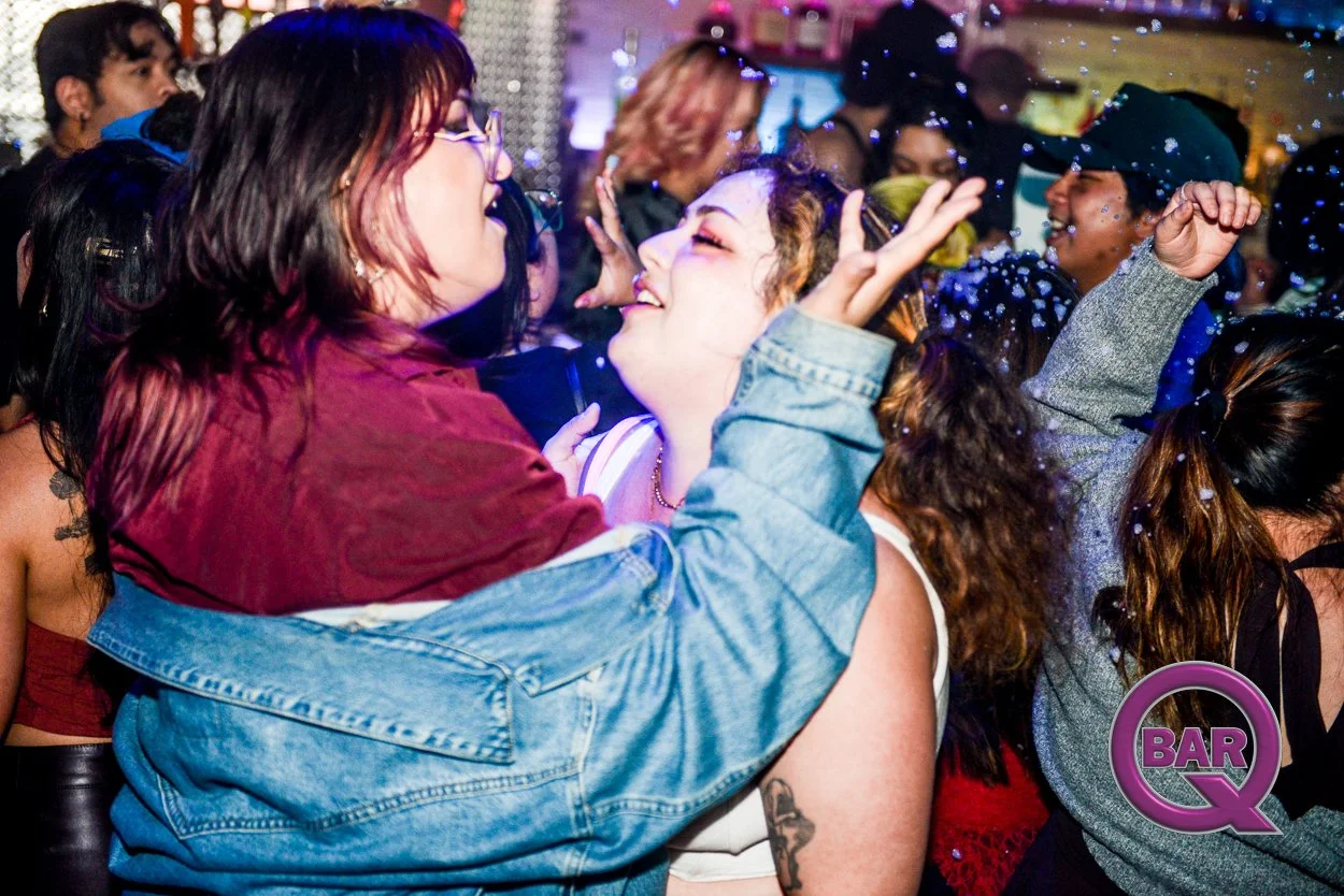 People dancing and enjoying themselves at a crowded party or nightclub with colorful lighting and a logo that says 'Bar Q'.