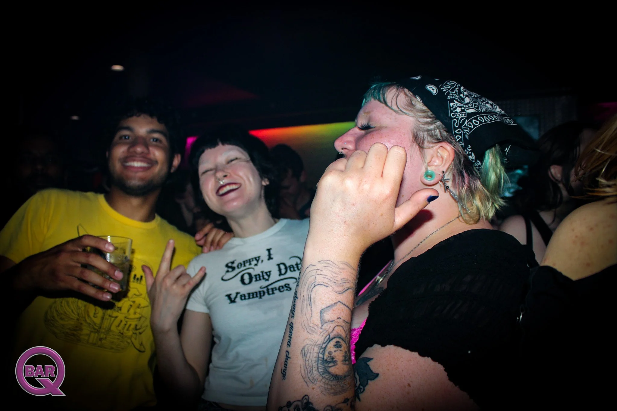 Group of people at a bar or party, smiling and enjoying themselves, with neon lights in the background.