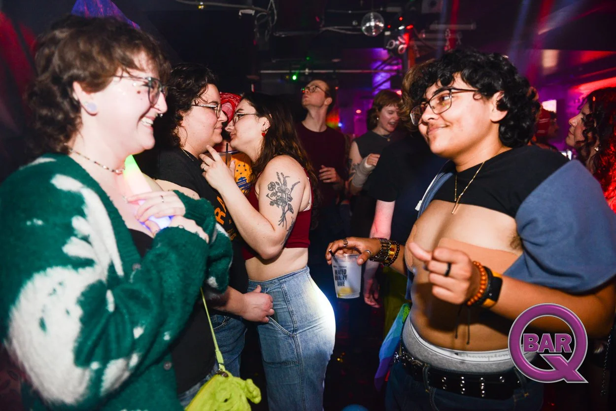 People dancing and socializing in a lively nightclub with colorful lighting, one person holding a drink, and a visible logo 'BAR Q' in the bottom right corner.